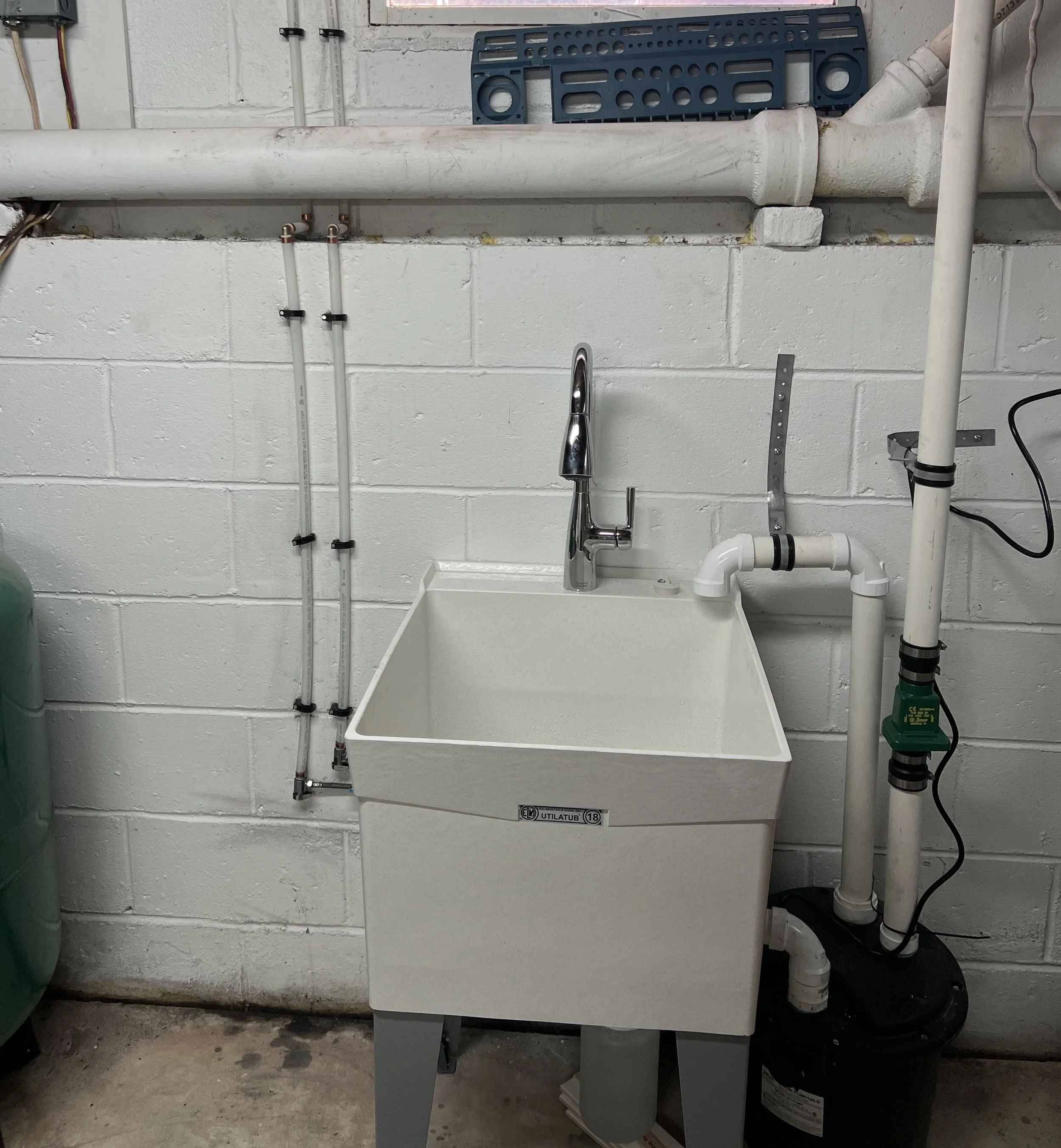Close-up of a dripping outdoor white PVC pipe connection wrapped with a dirty plastic bag, against a brick wall background with some green foliage.