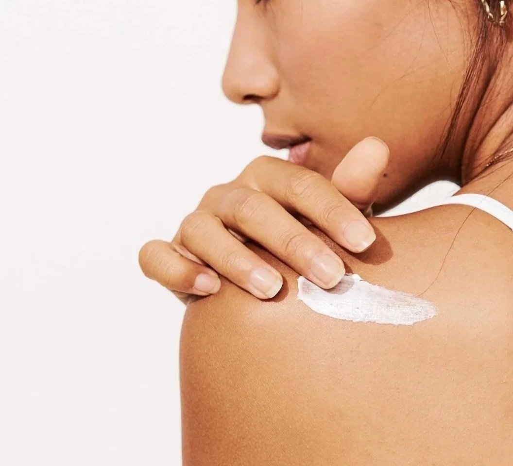 A woman applying skincare lotion to her shoulder with her hand.