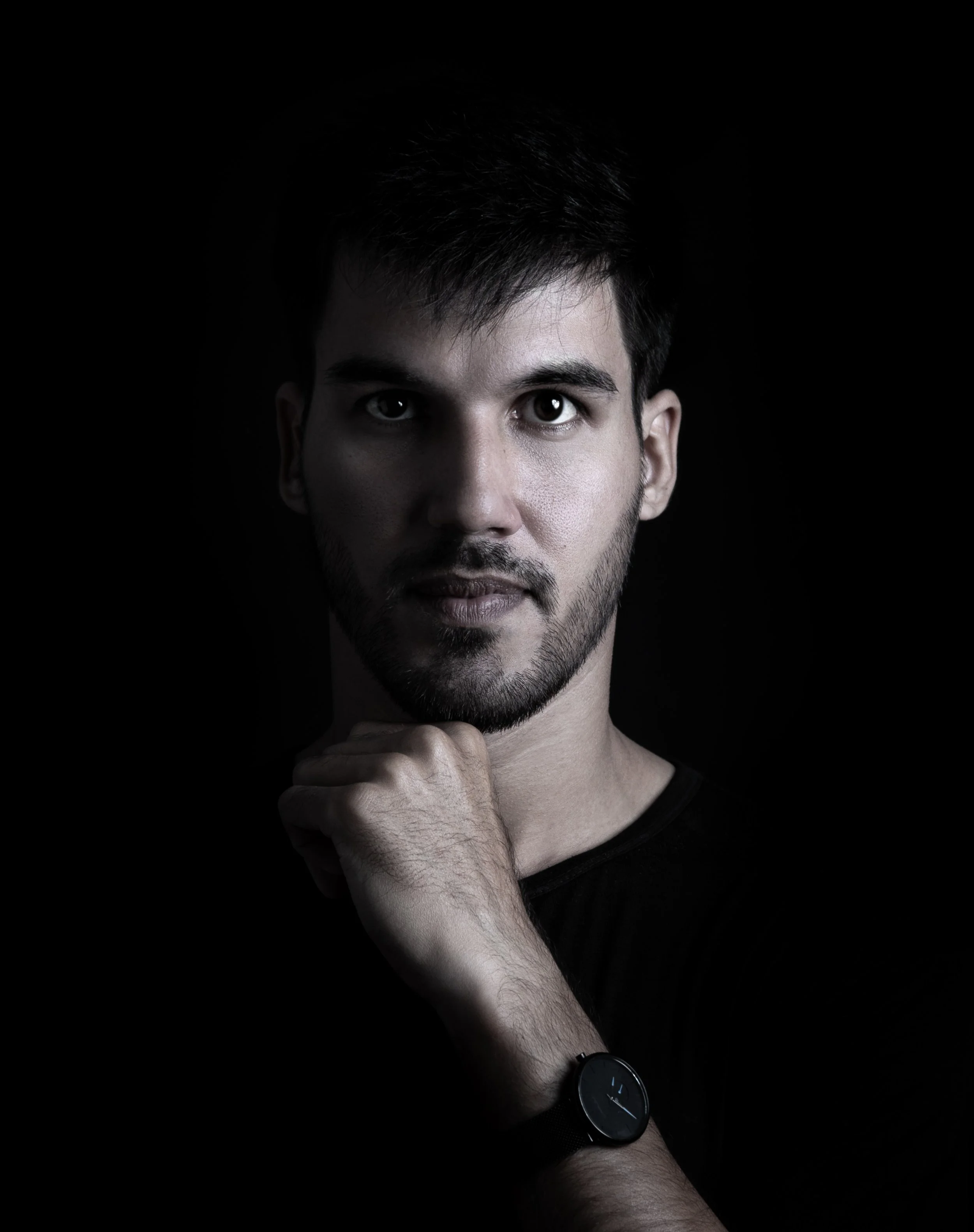 Retrato de un hombre joven con barba, gesticulando con la mano y viendo a la cámara con fondo negro.