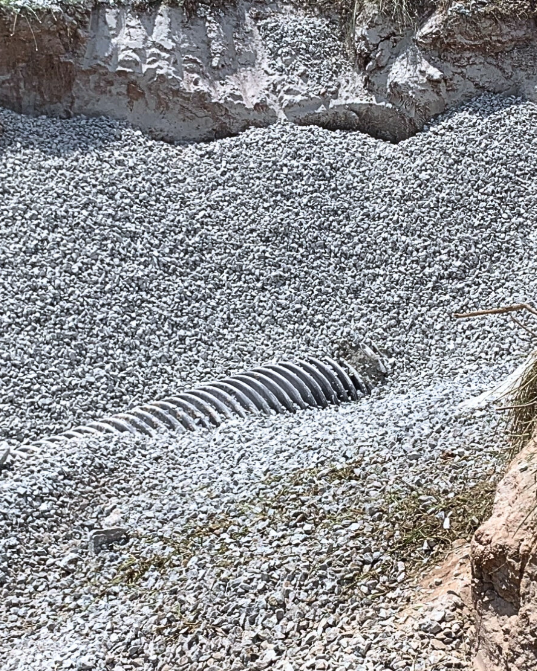 A corrugated pipe lying in gravel at the base of a rocky cliff.