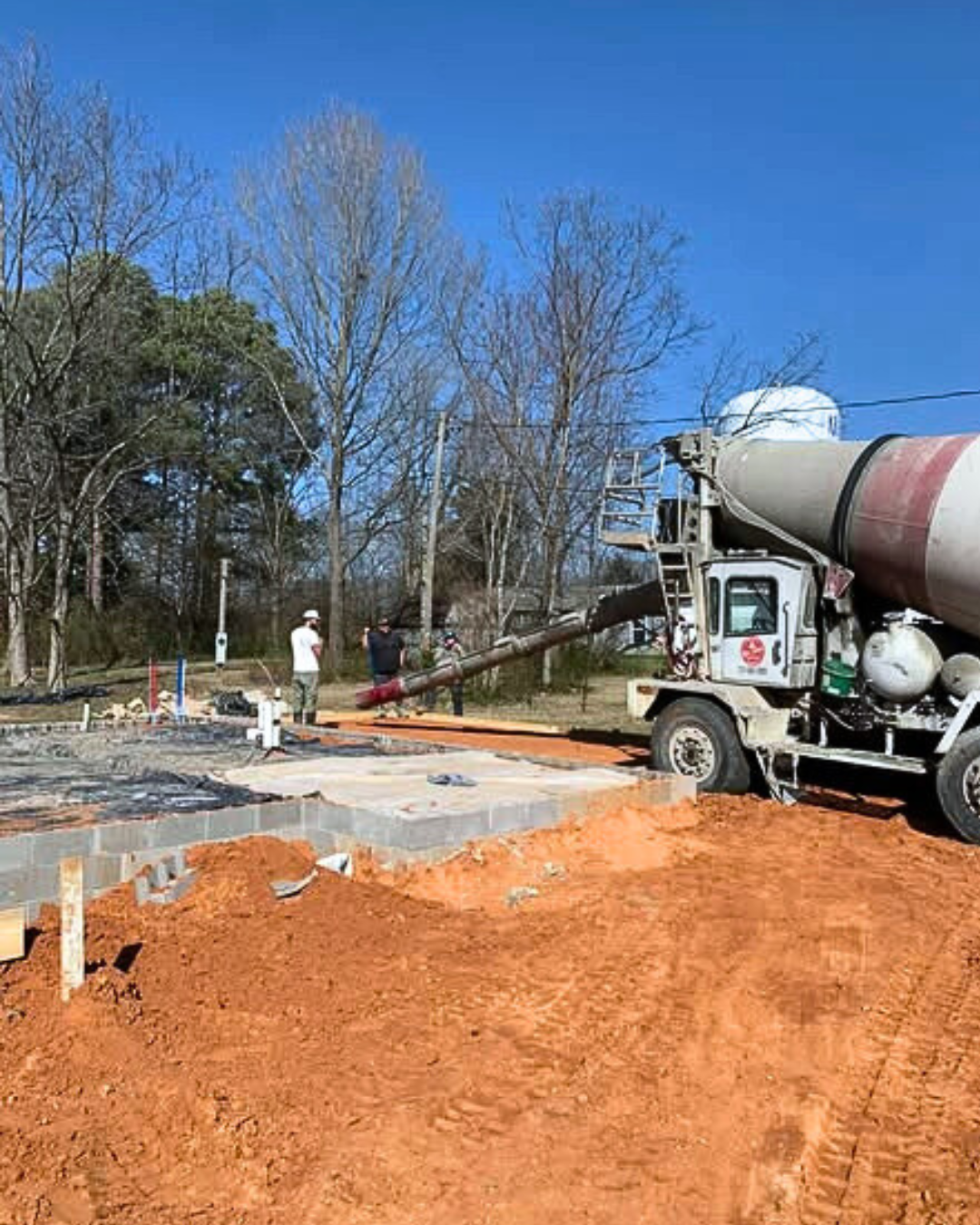 Construction site with workers, a cement mixer truck, and concrete being poured onto the ground.