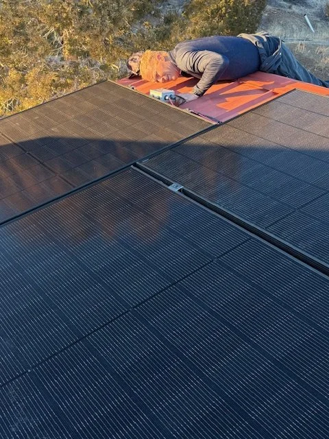 A person inspecting solar panels on a roof during sunset.