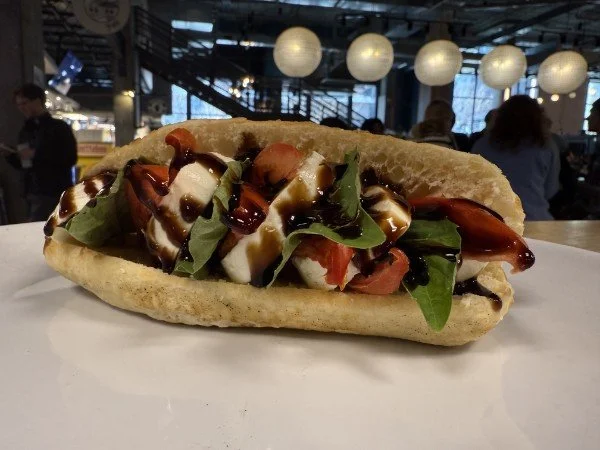 Italian sub sandwich with bread, lettuce, tomato, cheese, and balsamic glaze.