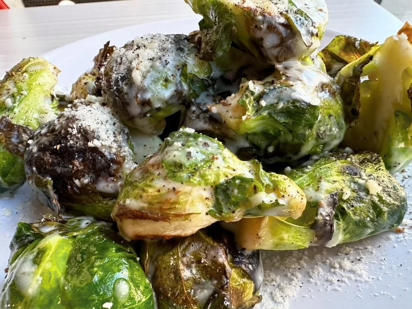 Charred Brussels sprouts with melted cheese, black pepper, and powdered seasoning on a white plate.