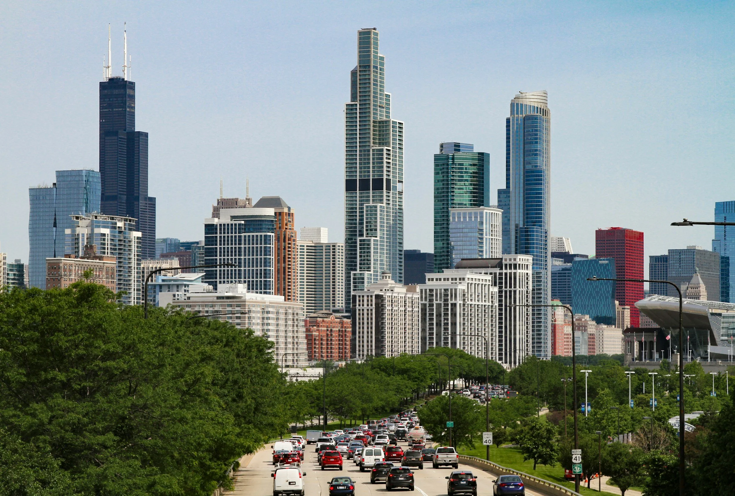 View of Chicago skyline with tall skyscrapers and a busy street with cars and trees in the foreground.