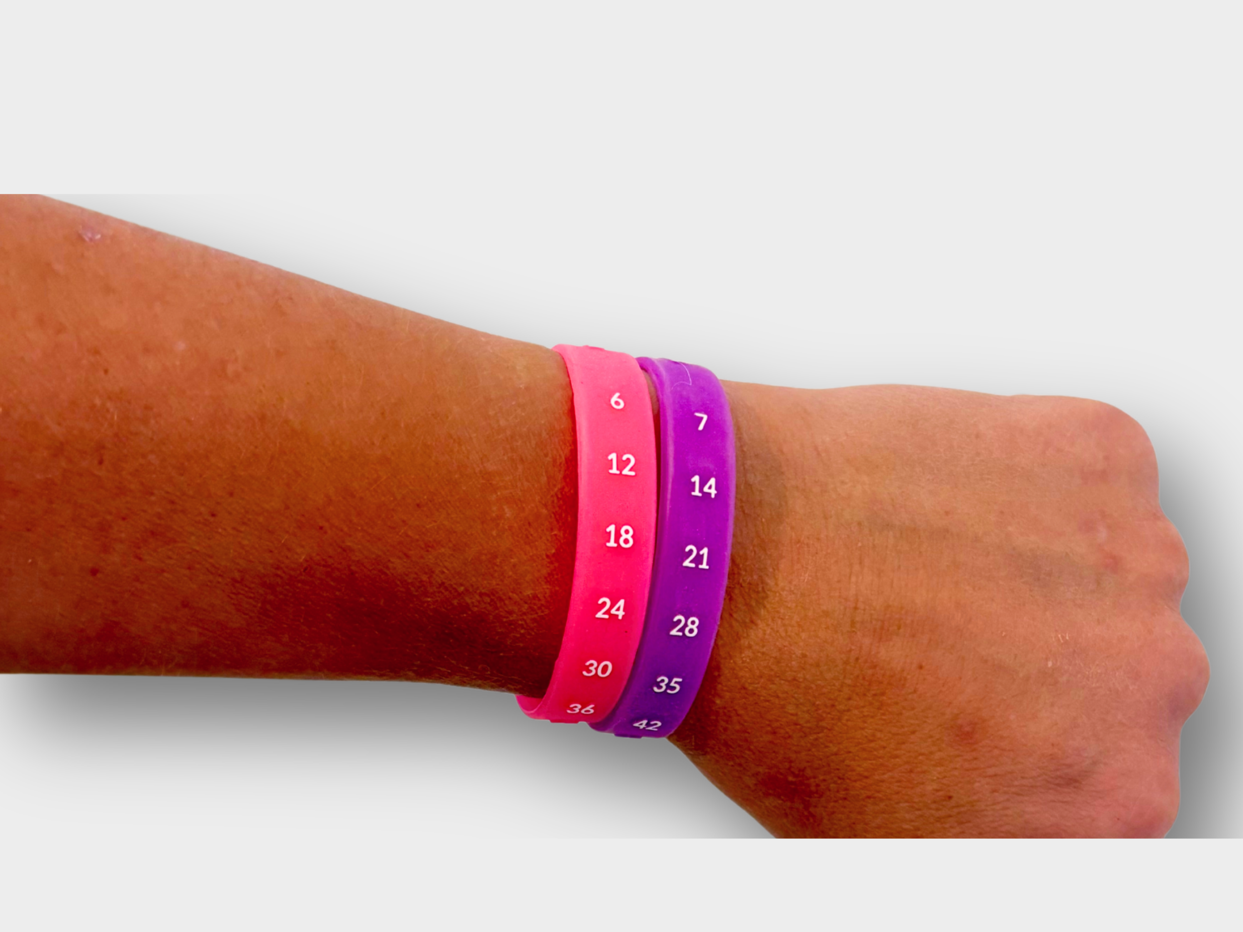 Person's arm wearing two silicone wristbands, one pink and one purple, with skip counting patterns of 6s and 7s printed on them.