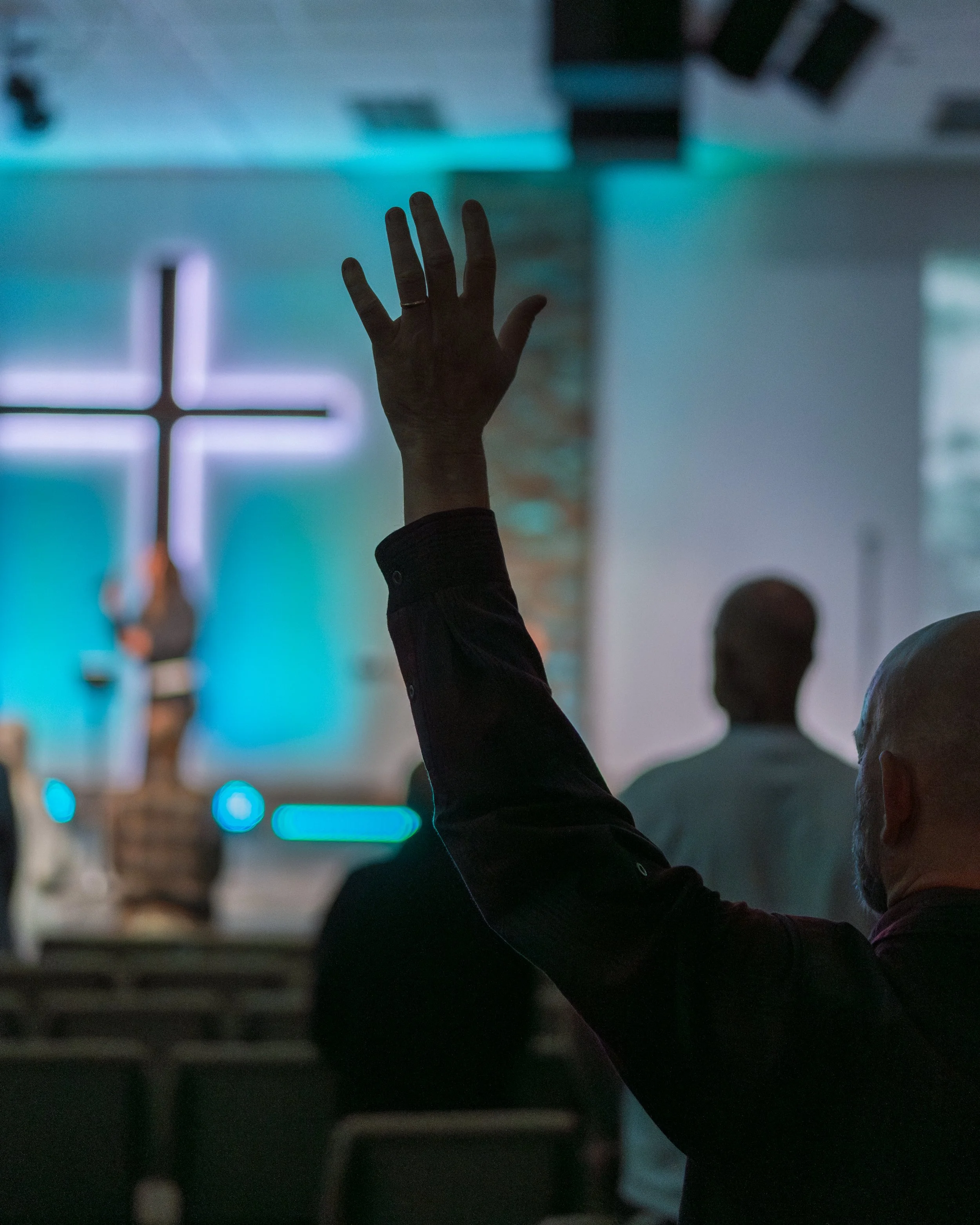 A person raising their hand inside a church with a lit cross in the background.