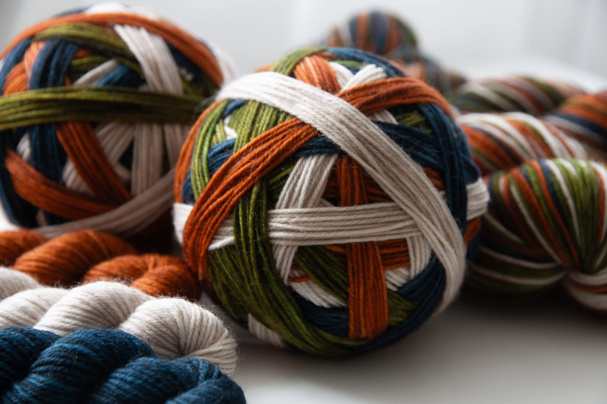 Self-striping yarn balls, with one self-striping ball at the center, along with other balls of contrasting mini-skeins including white, blue, orange, and striped, on a white surface.