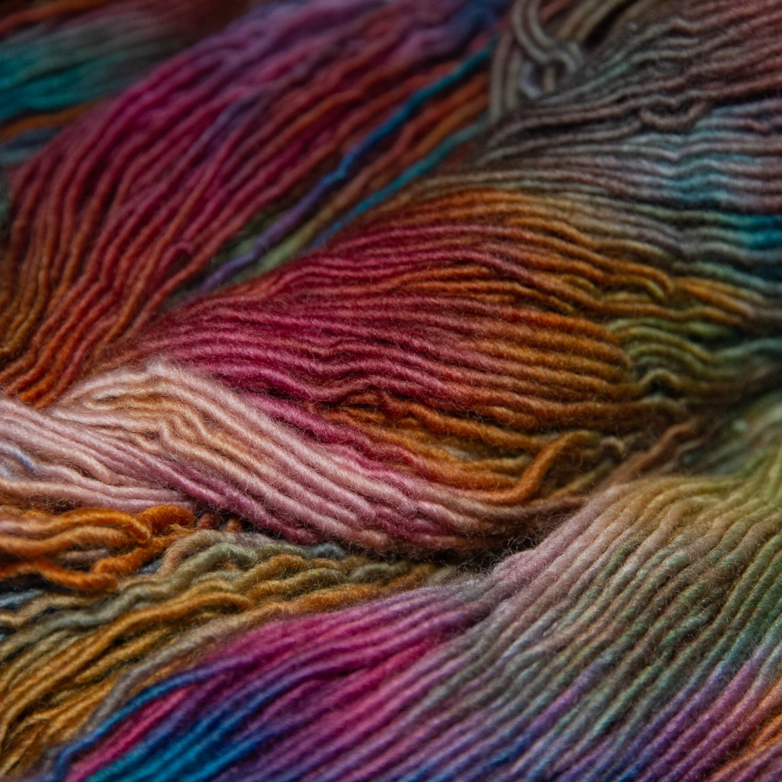 Close-up of variegated hand-dyed yarn strands in shades of pink, orange, blue, green, and purple.