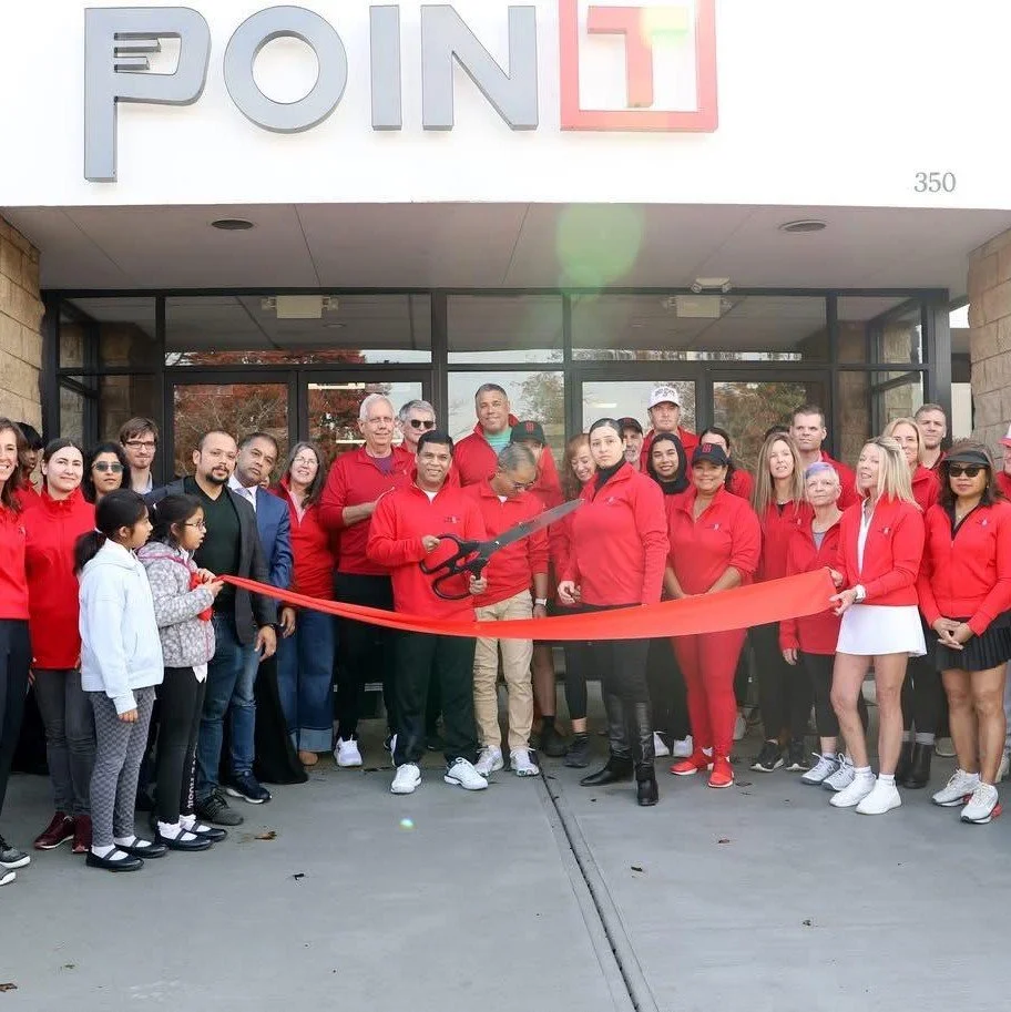 Group of people gathered outside a building for a ribbon-cutting ceremony, with some holding large scissors and a red ribbon.