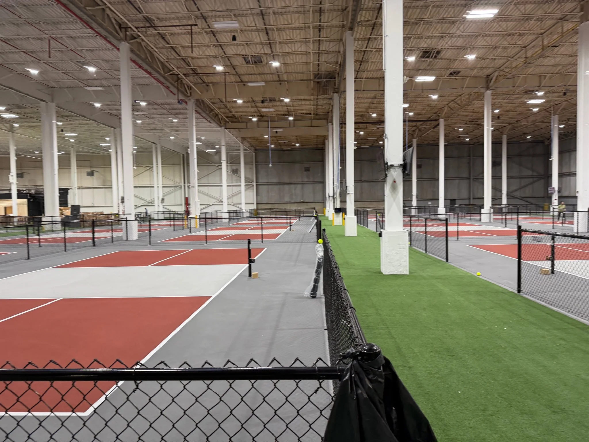 Indoor courts with red and blue playing surfaces, surrounded by black fencing and illuminated by overhead lights.