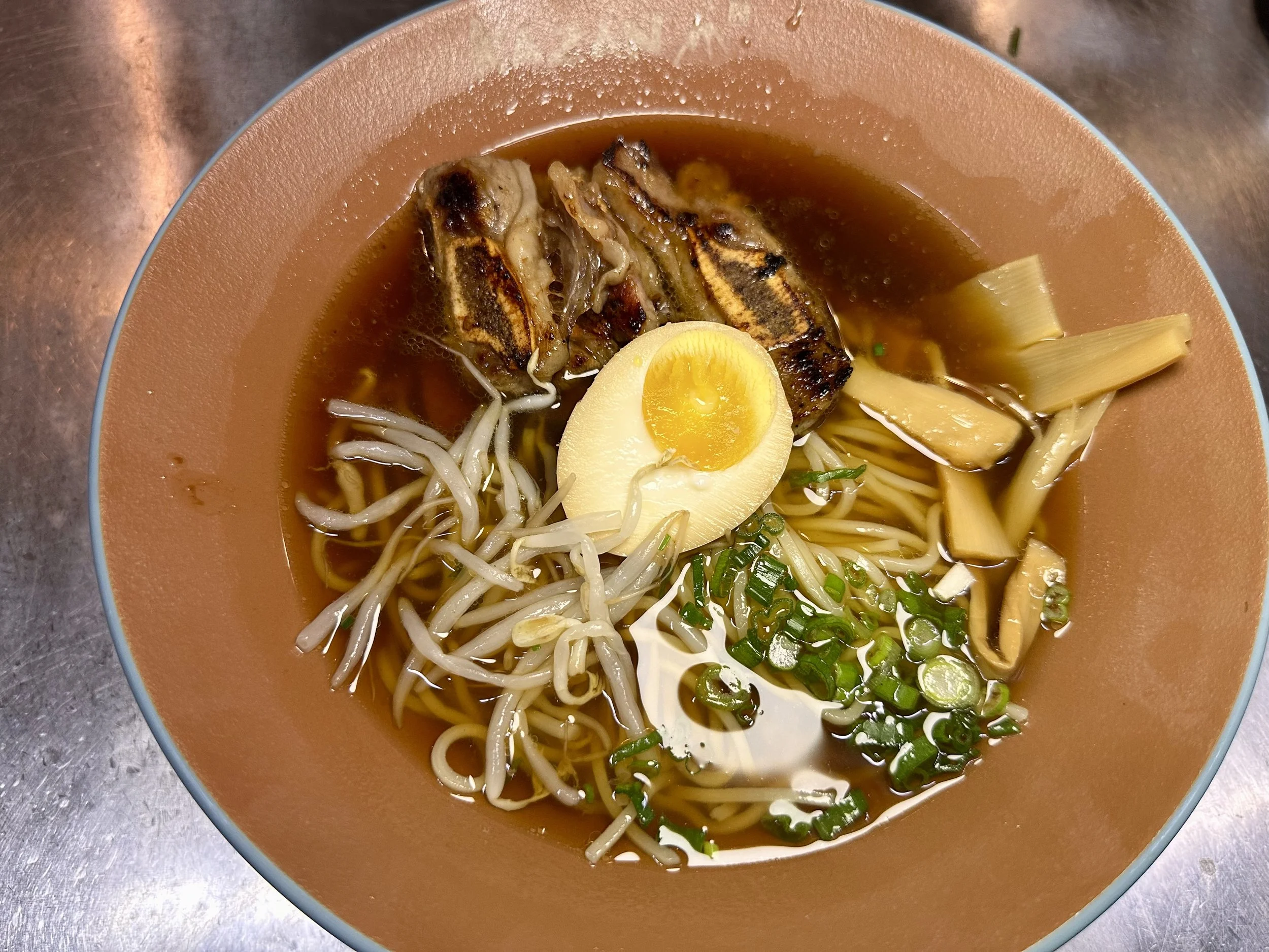 Bowl of ramen with boiled egg half, grilled meat, bean sprouts, green onions, and bamboo shoots in broth.