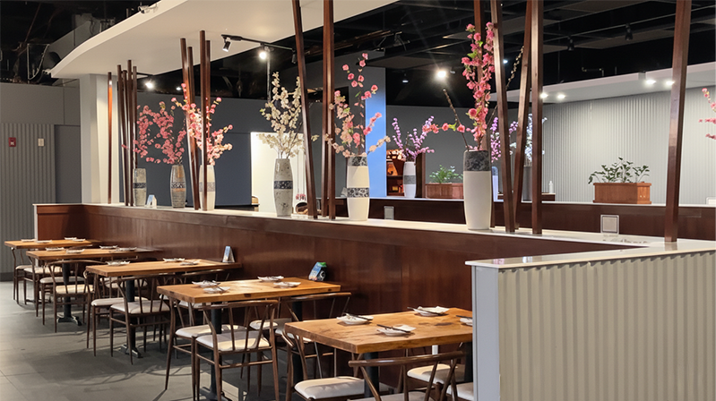 Empty restaurant with wooden tables and chairs, decorated with vases of pink and white cherry blossoms.