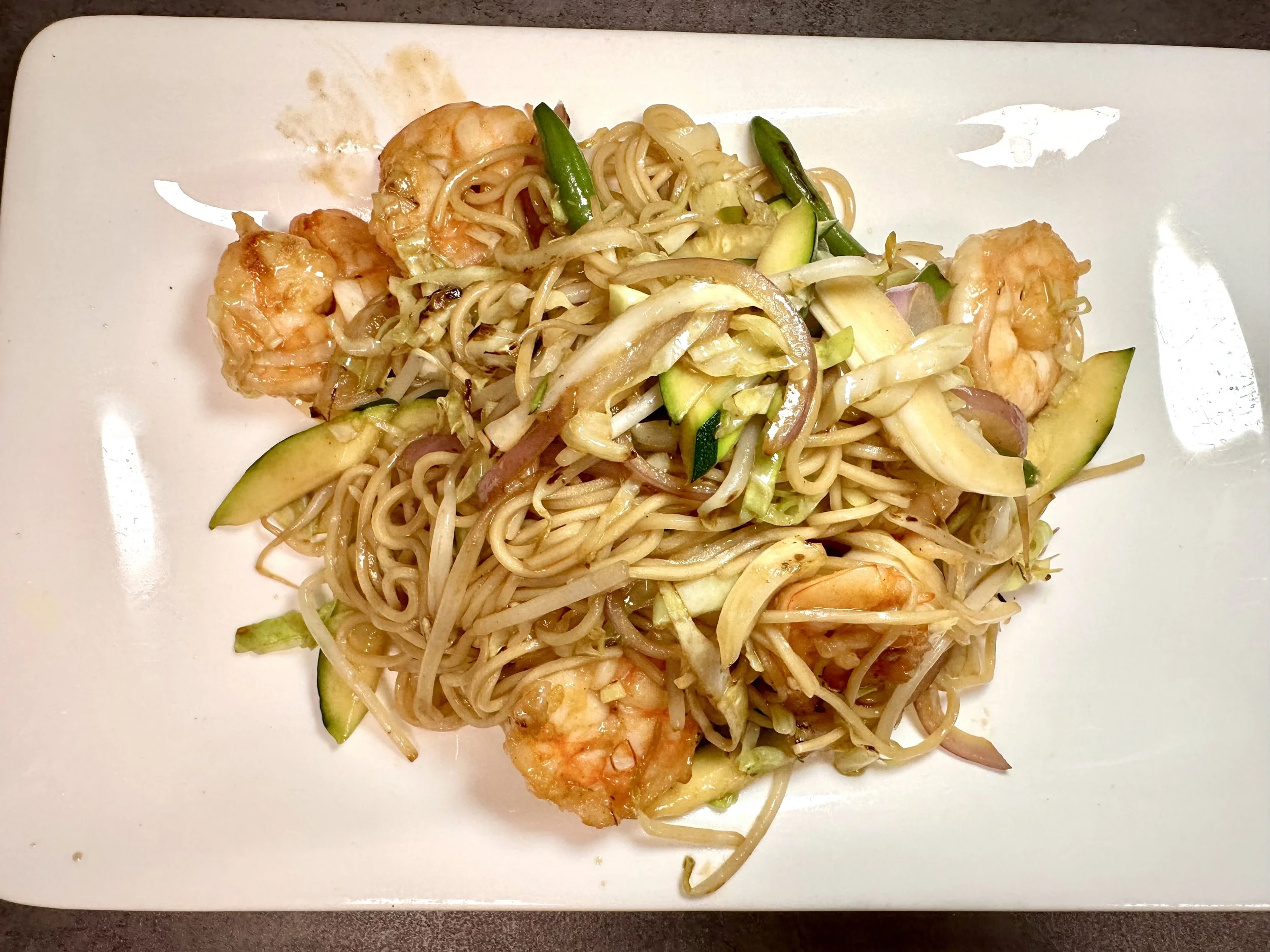 Shrimp and vegetable fried noodles on a white plate.