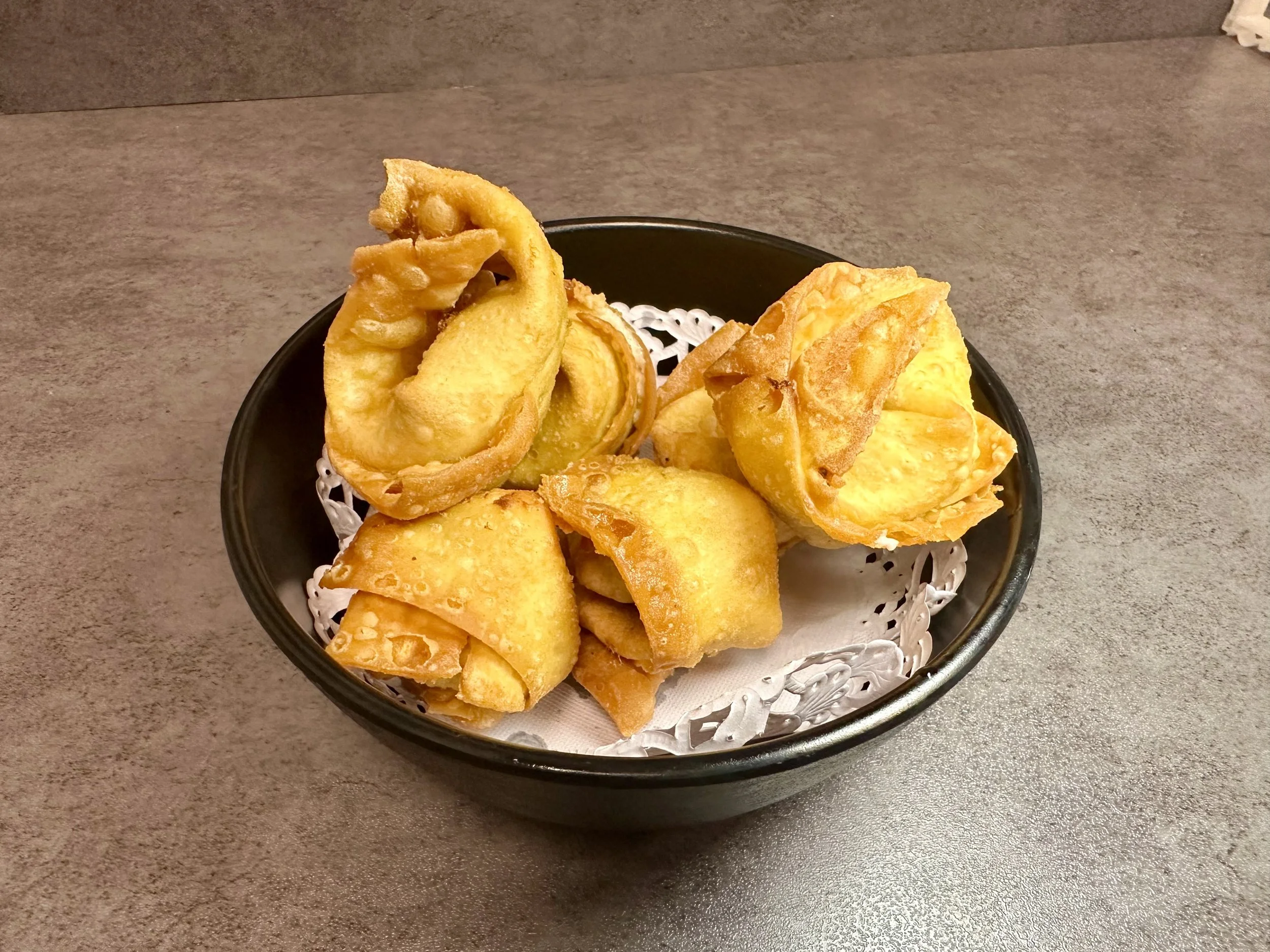 A black bowl containing fried wontons on a gray surface.