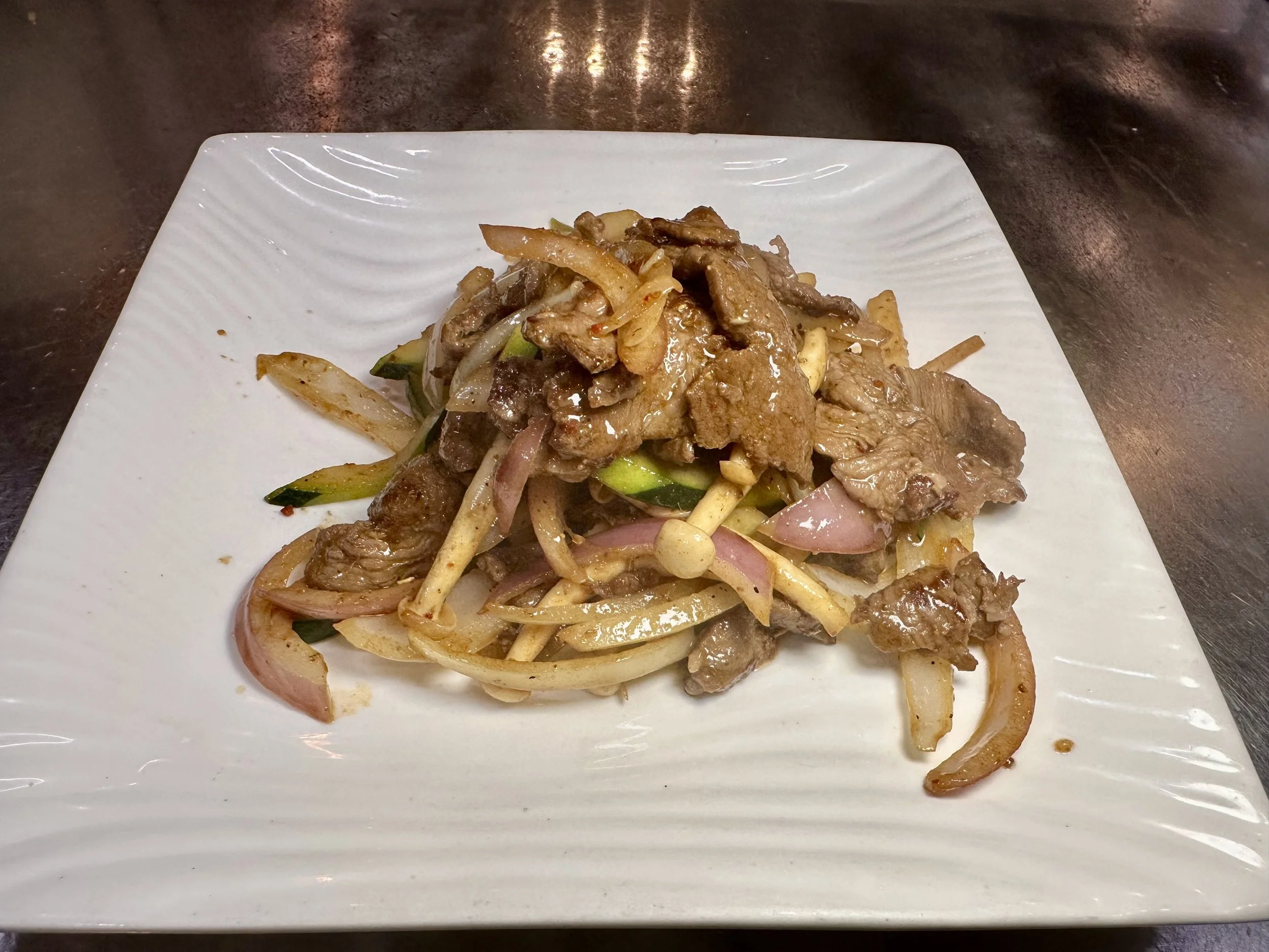 Stir-fried beef with onions, zucchini, and bean sprouts on a white square plate.