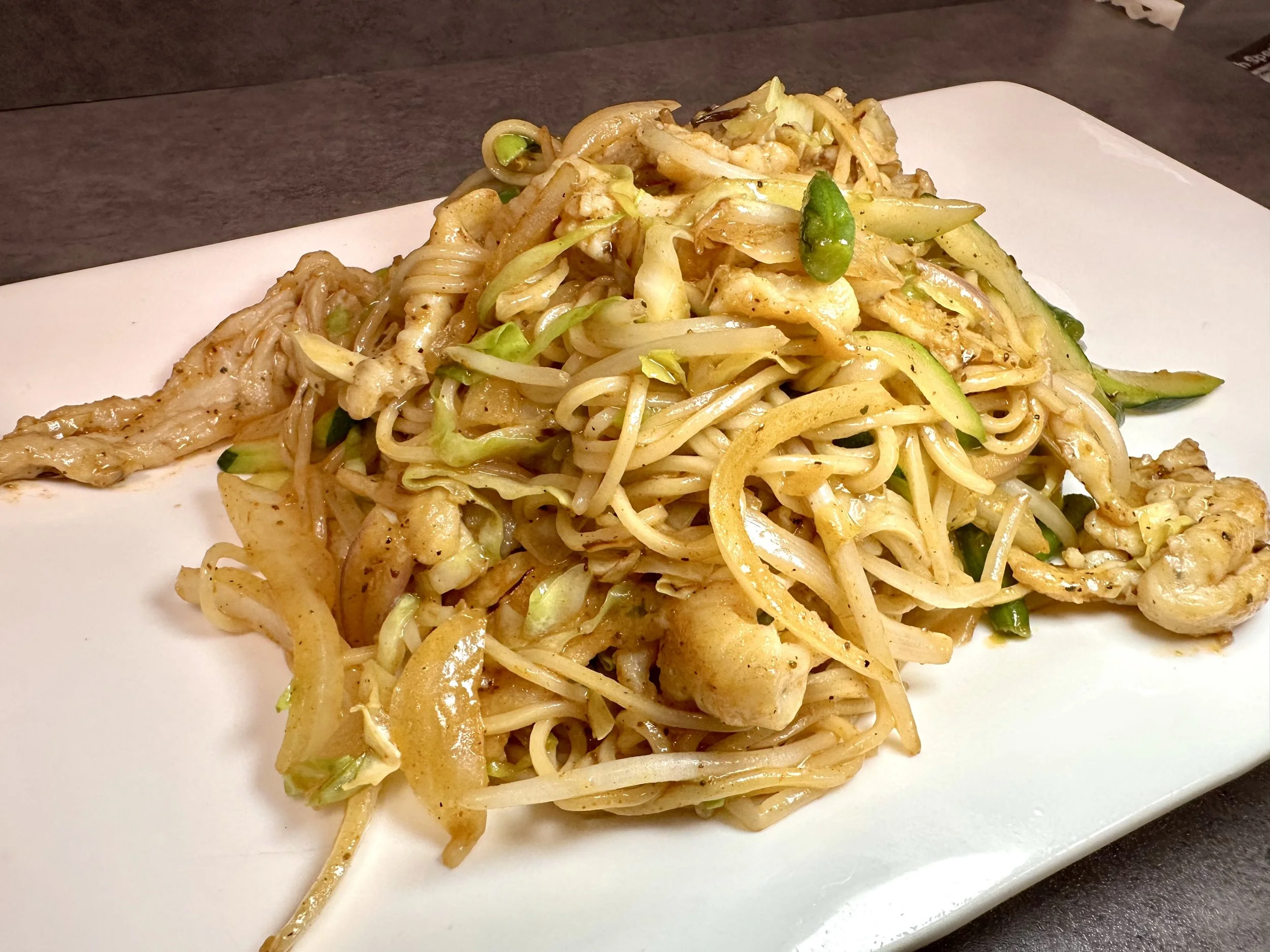 Stir-fried noodles with vegetables on a white plate.