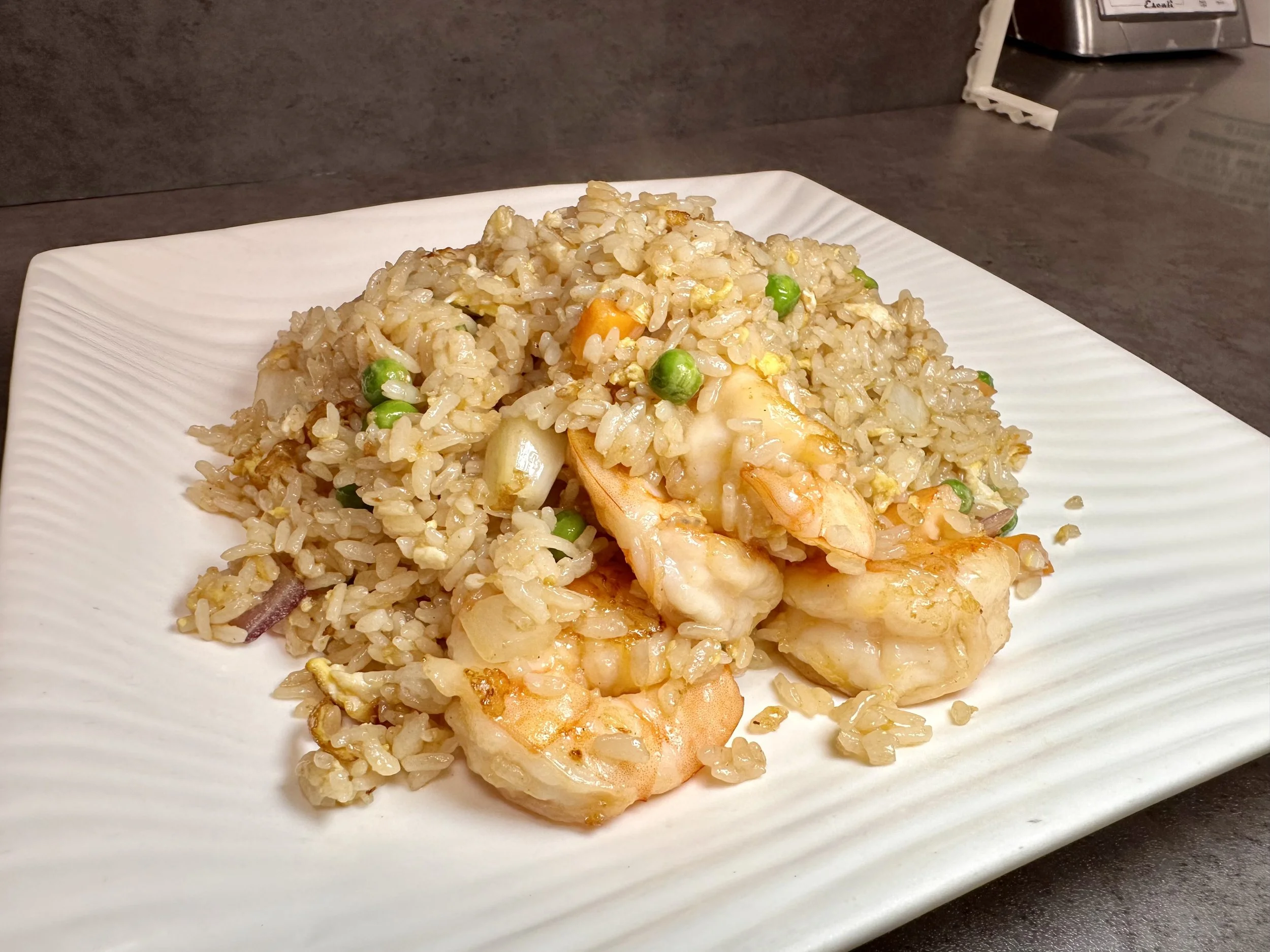 Plate of fried rice with shrimp, peas, carrots, and onions on a white rectangular dish.