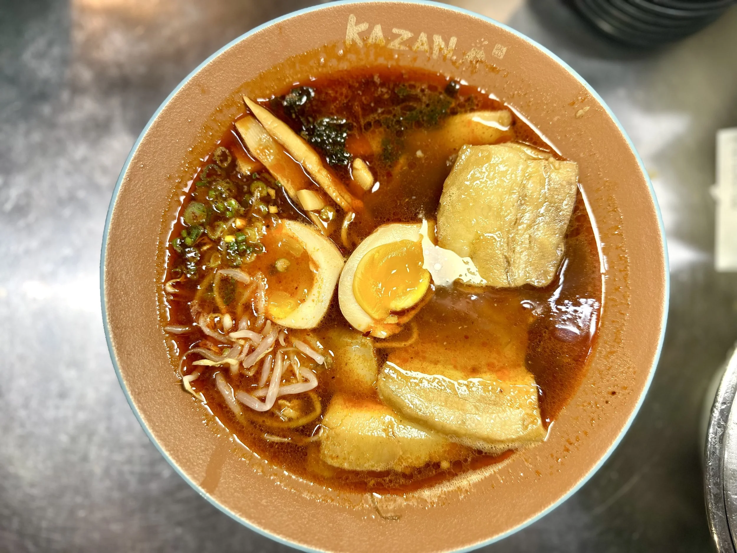 Bowl of ramen with soft-boiled egg, fried fish cake, bamboo shoots, seaweed, and green onions in a spicy broth.