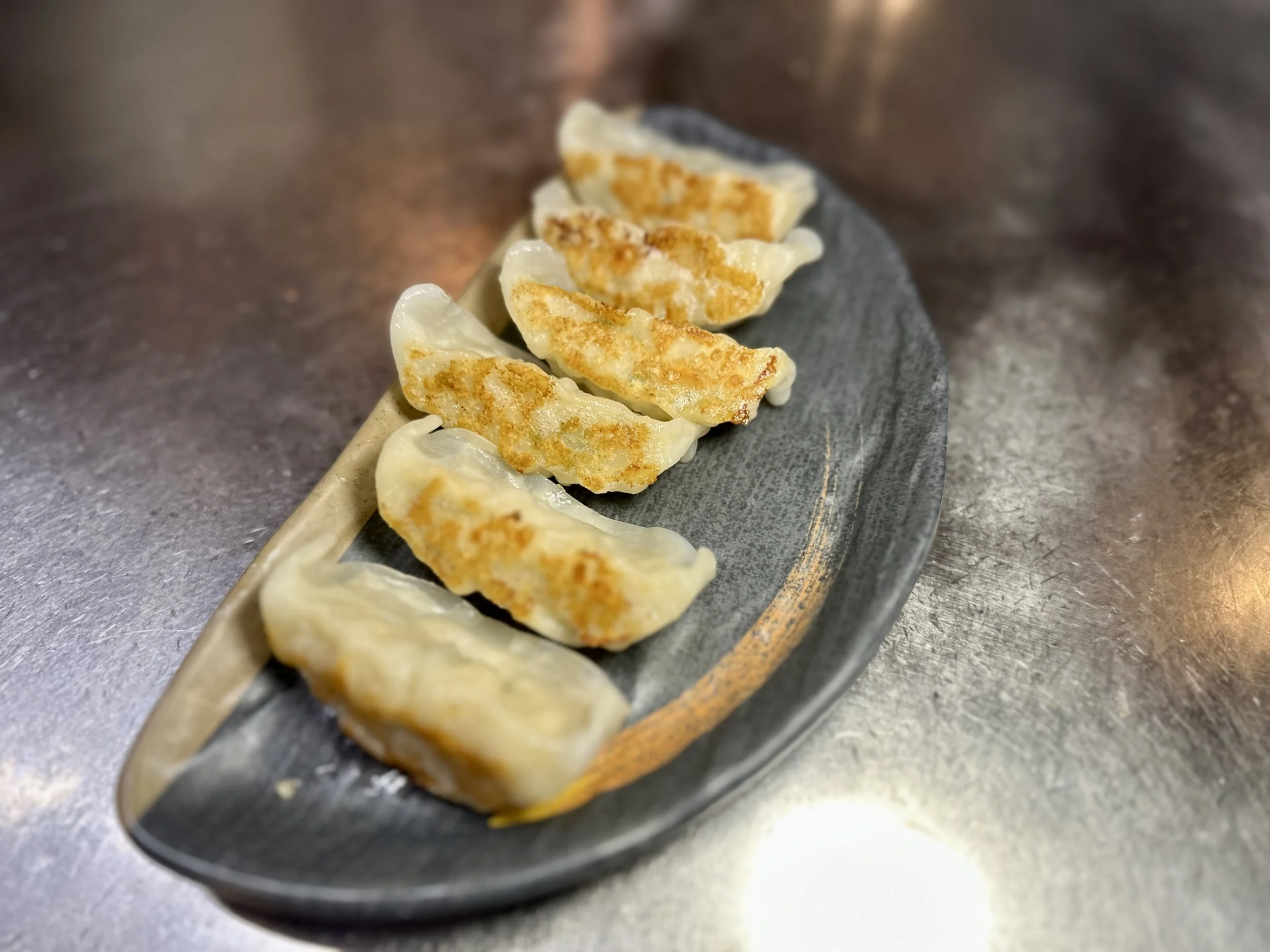 Six cooked dumplings arranged on a black oval plate placed on a stainless steel surface.