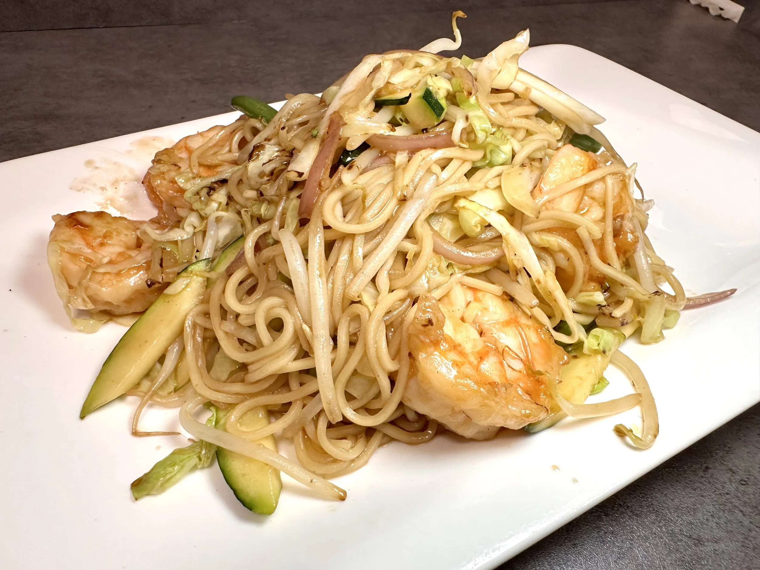 Plate of stir-fried noodles with shrimp, zucchini, and vegetables.