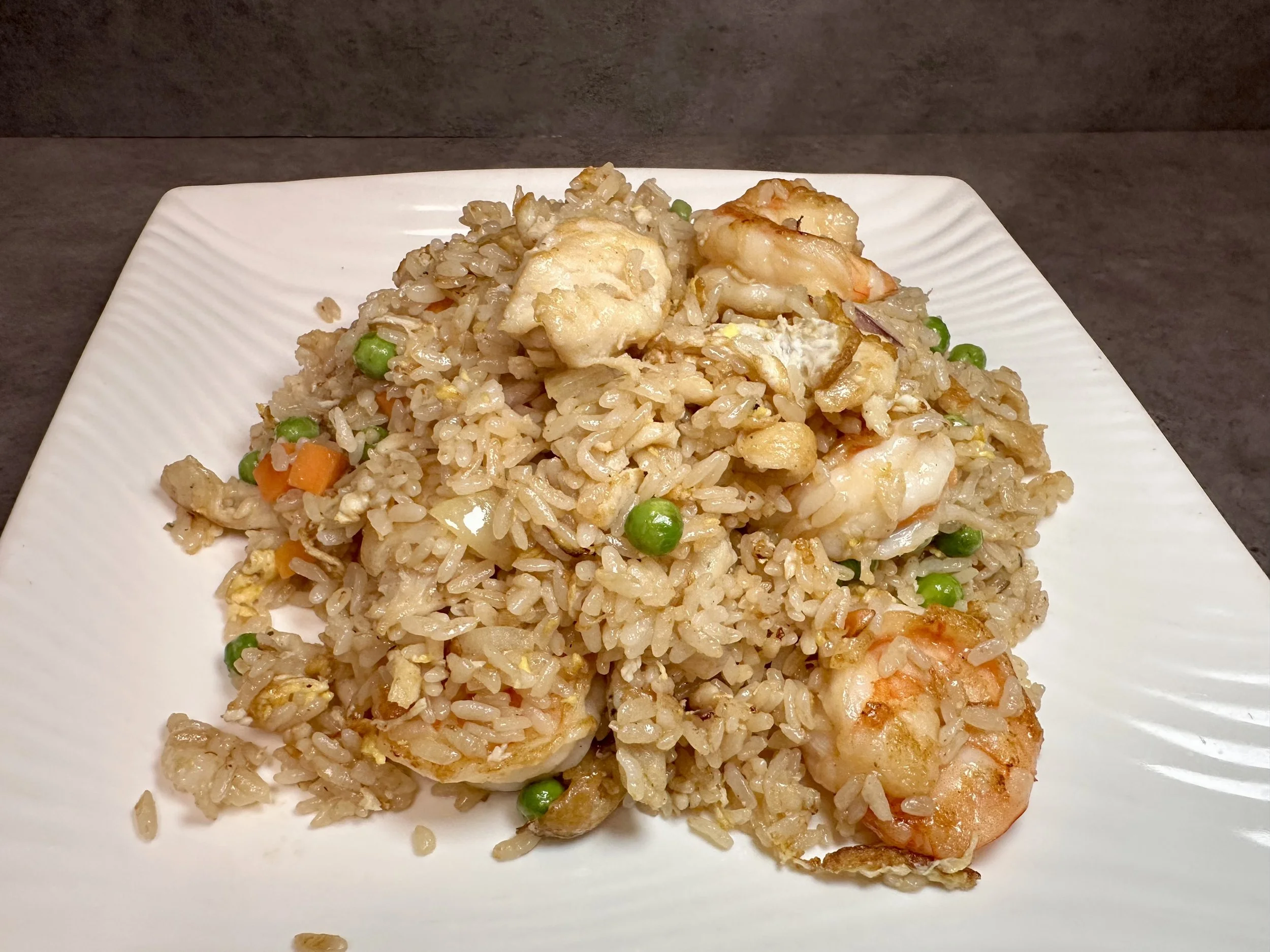 Plate of shrimp fried rice with peas, carrots, scrambled eggs, and rice on a white square plate.