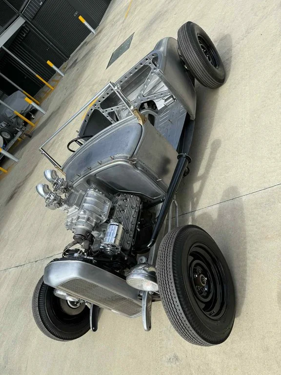 A partially assembled vintage race car on a concrete floor, showing the engine and chassis.