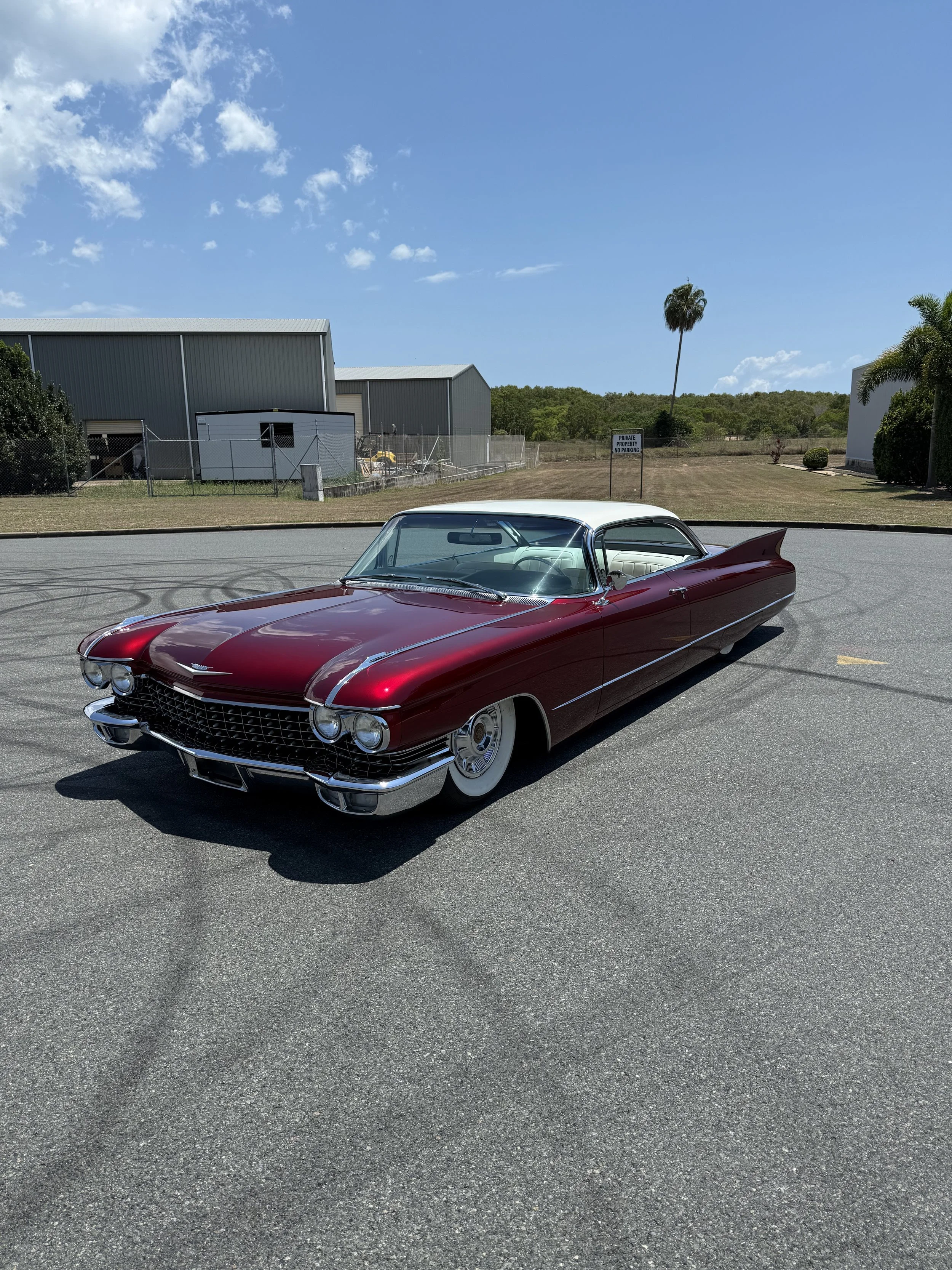 A vintage red and white Cadillac parked on an empty parking lot under a blue sky.