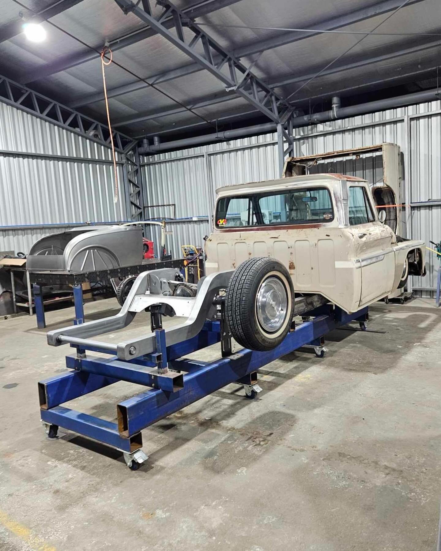 Disassembled vintage car body on a blue platform in a metal workshop.