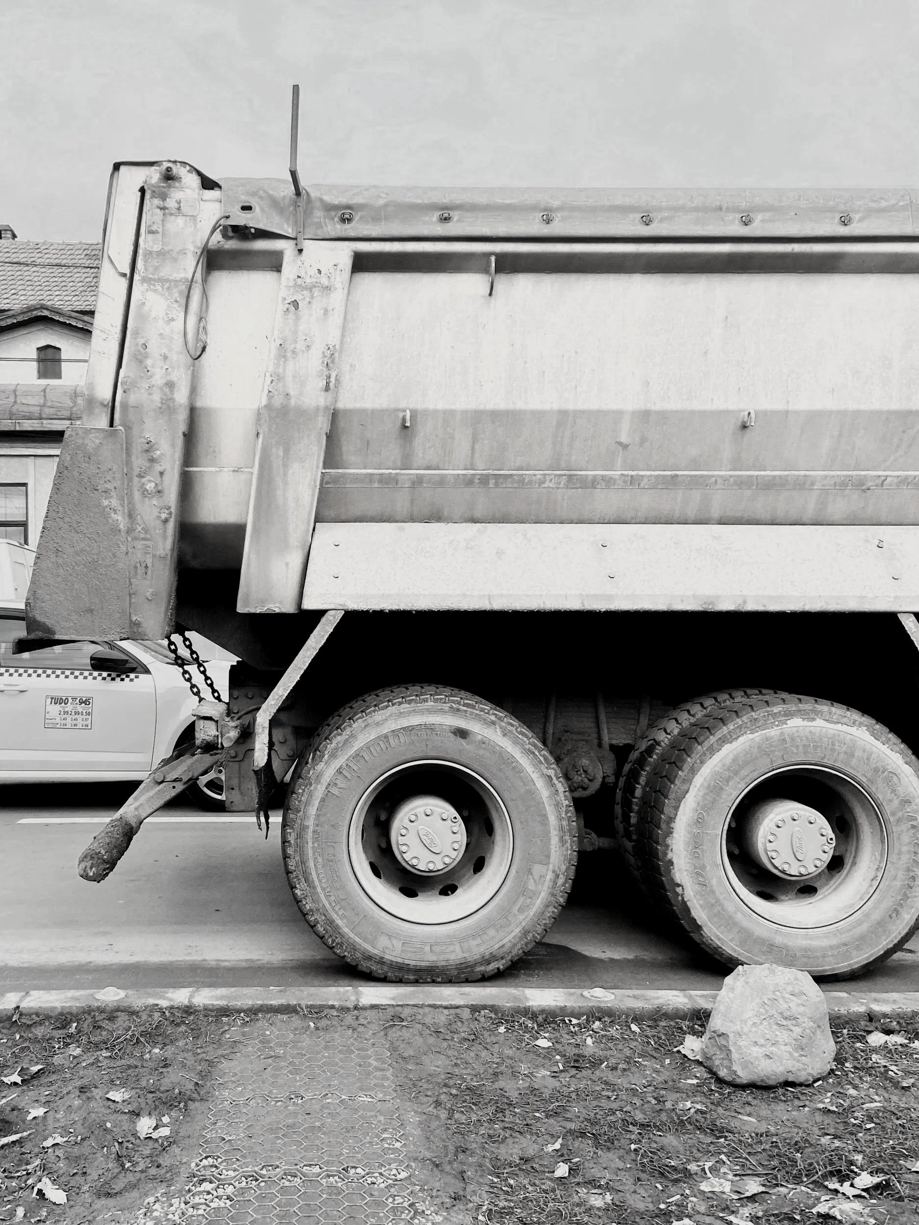 Black and white photo of a dump truck parked on a street, with a large rock and dirt in front of it.