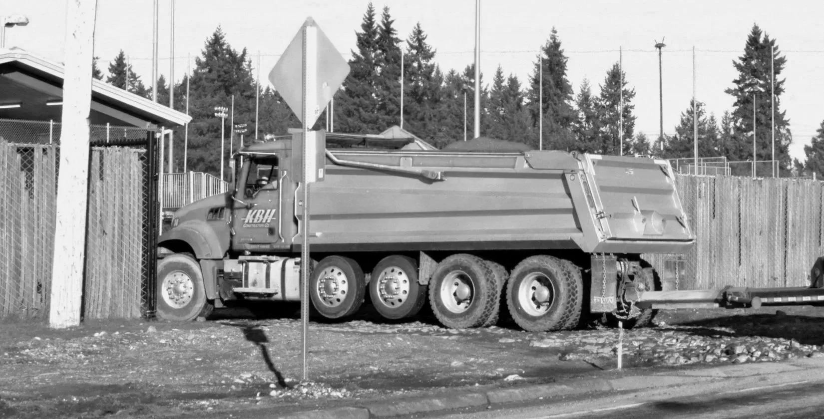 A large dump truck parked near a construction site with fencing and trees in the background.