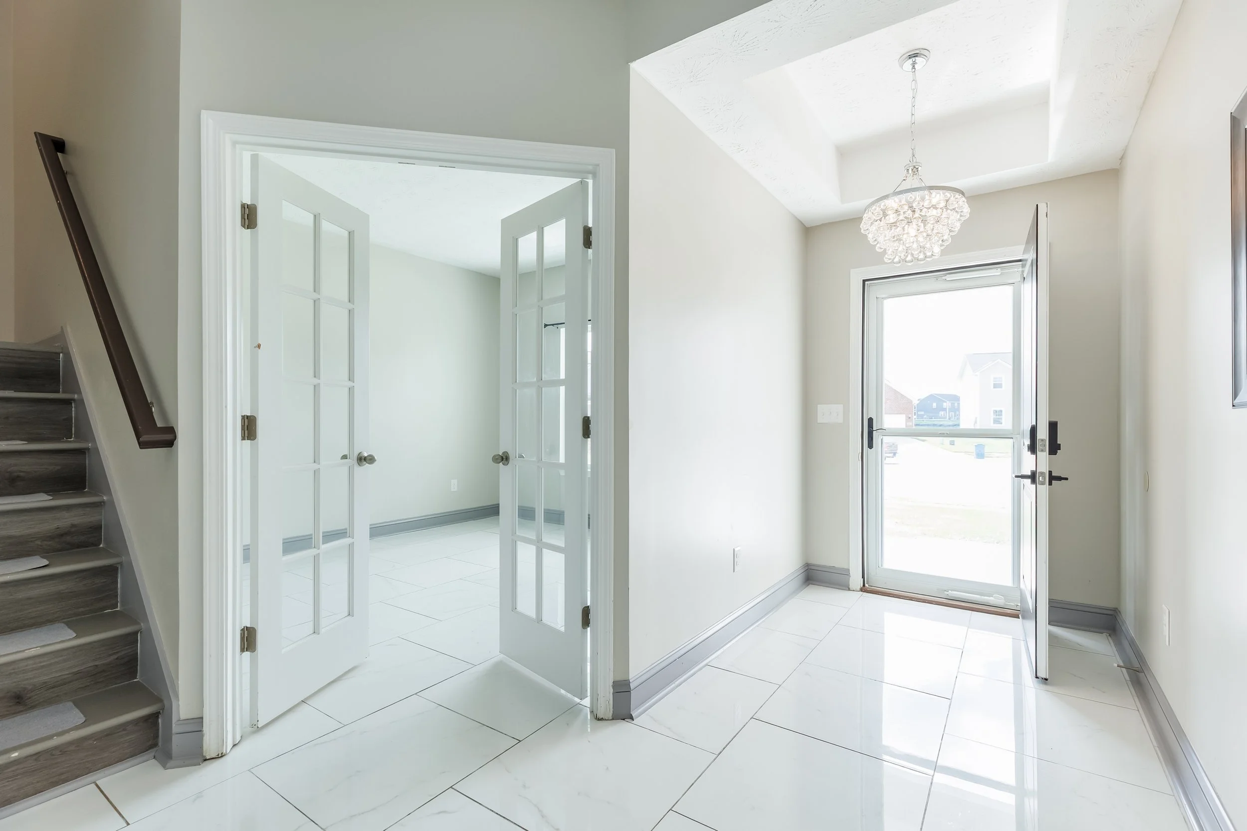 Entryway with white tile floor, glass double doors, and a windowed door leading outside, chandelier, and staircase