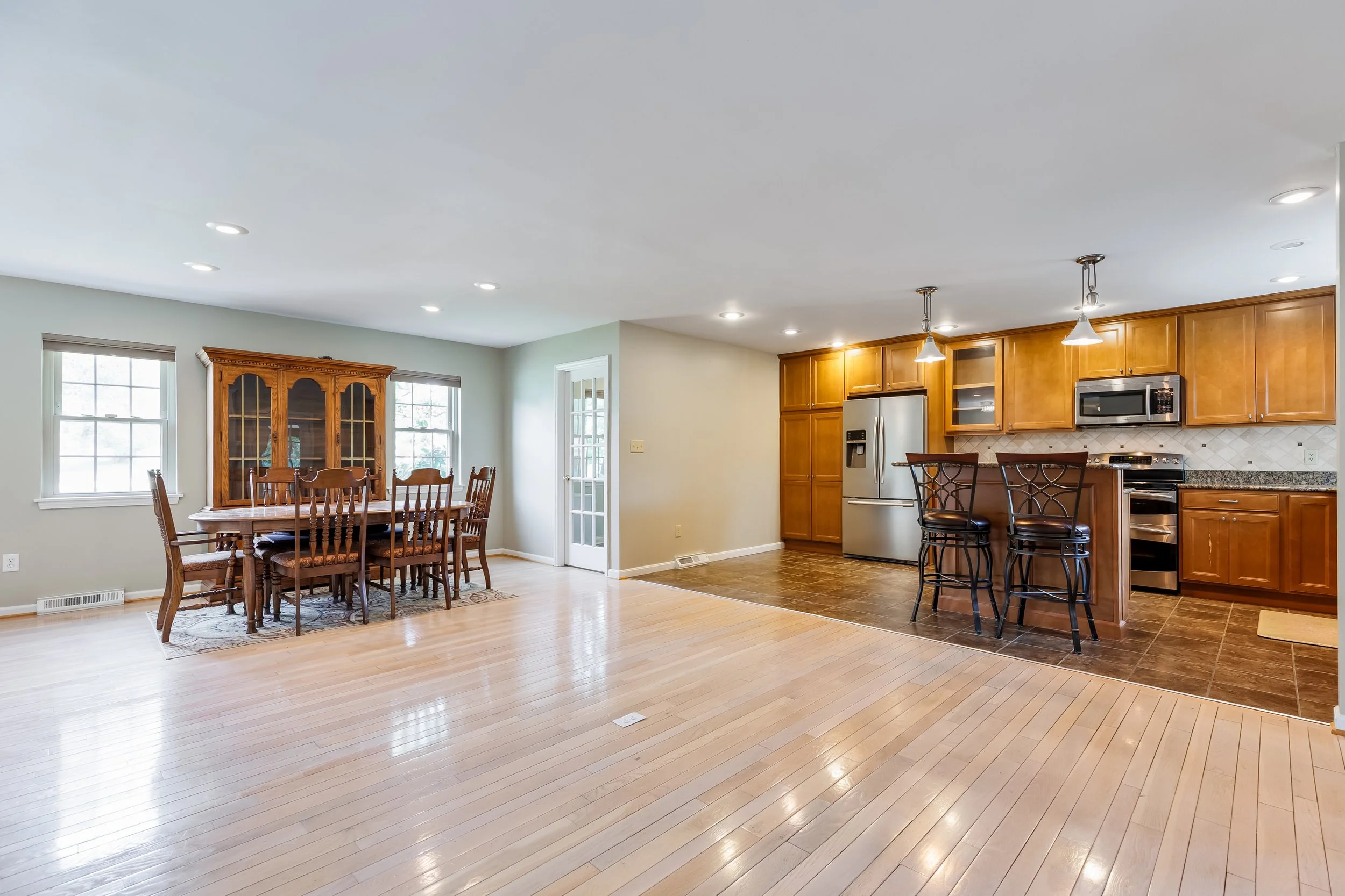 Open-concept kitchen and dining area with hardwood floors, wooden cabinets, stainless steel appliances, and a dining table with chairs.