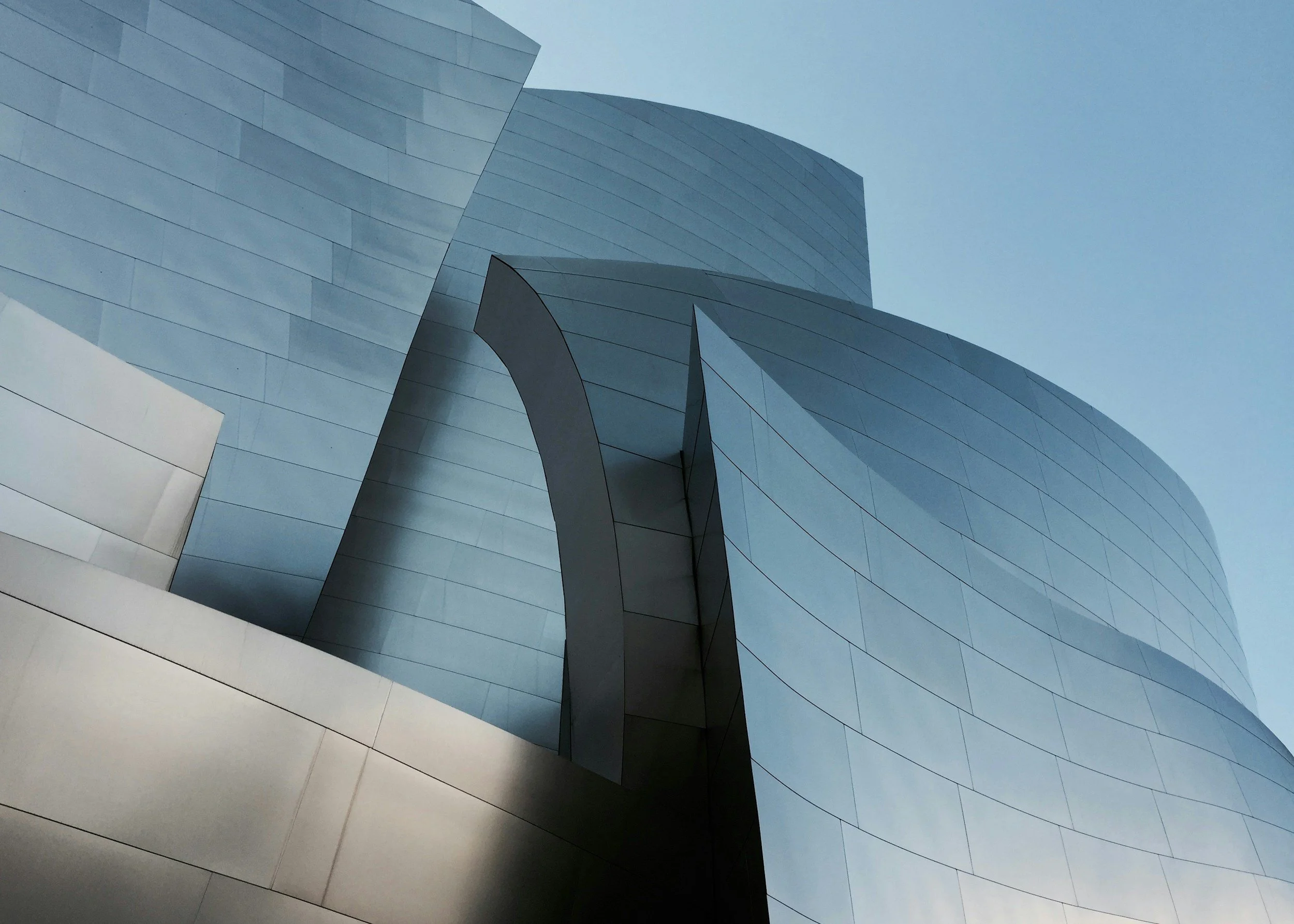 Modern architectural building with smooth, metallic, curved surfaces and a sky background.