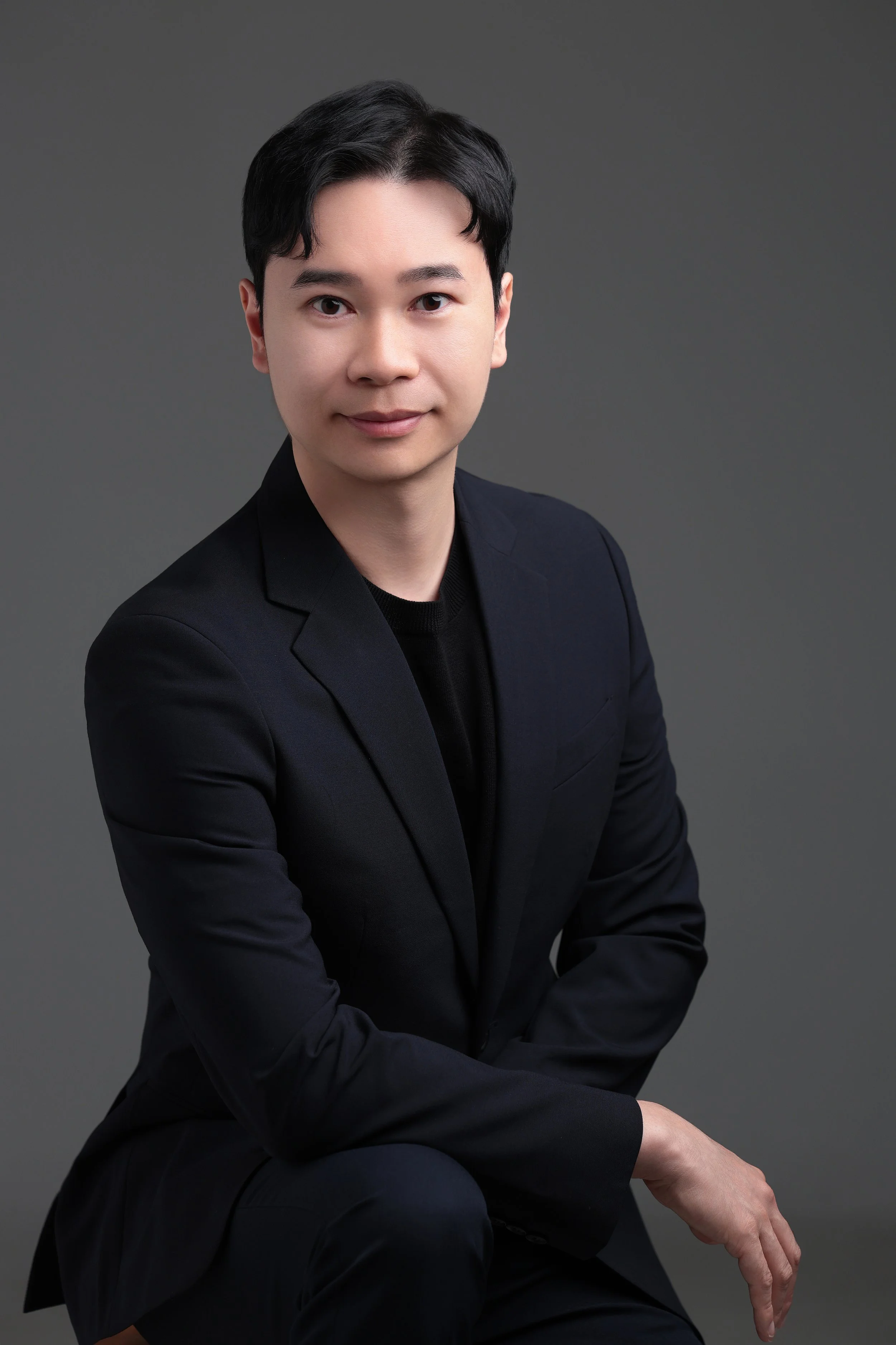 Doctor, Hong Kong, Canada, China, Good looking, smart, helpful, good doctor, collagen doctor, best doctor, singapore's best, longevity, aesthetics, Portrait of a young man with black hair, wearing a black blazer, seated against a gray background.