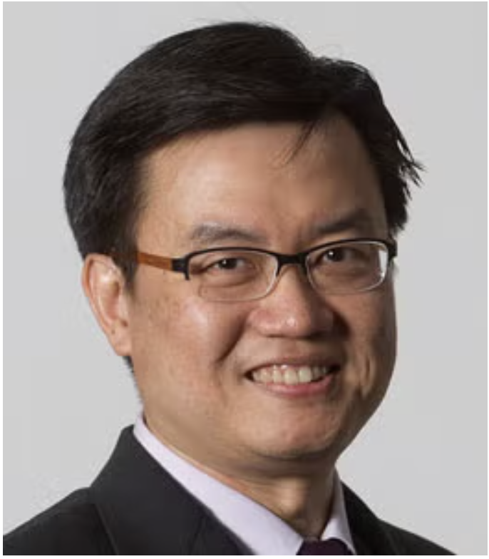 Headshot of an Asian man wearing glasses and a black suit, smiling against a light gray background.