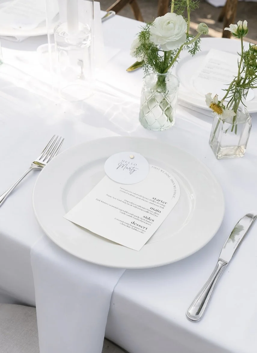Elegant table setting with a white plate, a menu card and place card for a wedding or bachelorette dinner party.