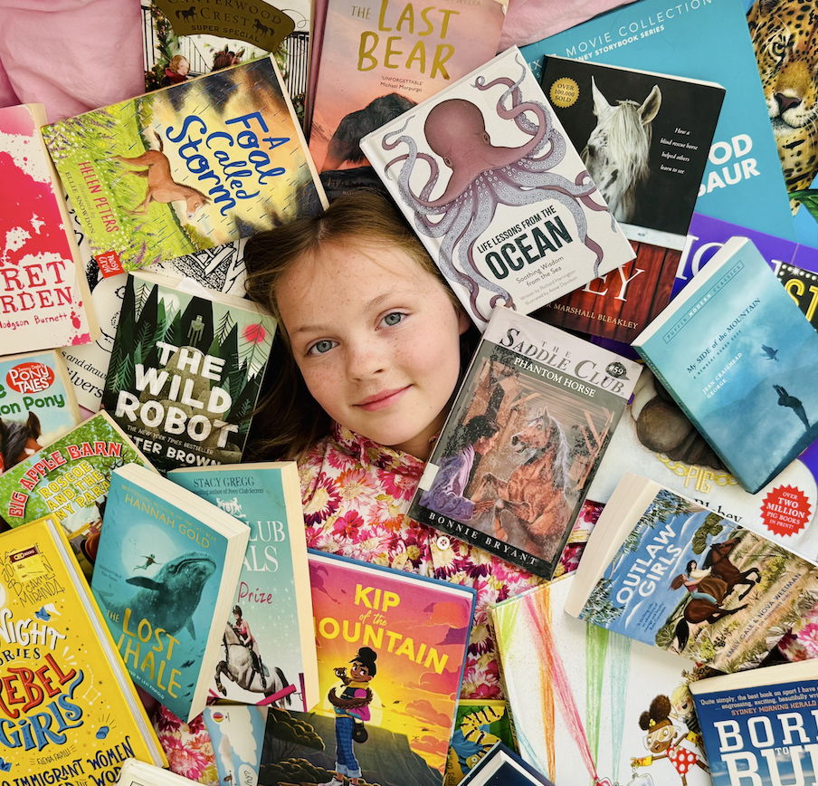 Young girl lying on a bed surrounded by colorful children's books with various animal and adventure themes.