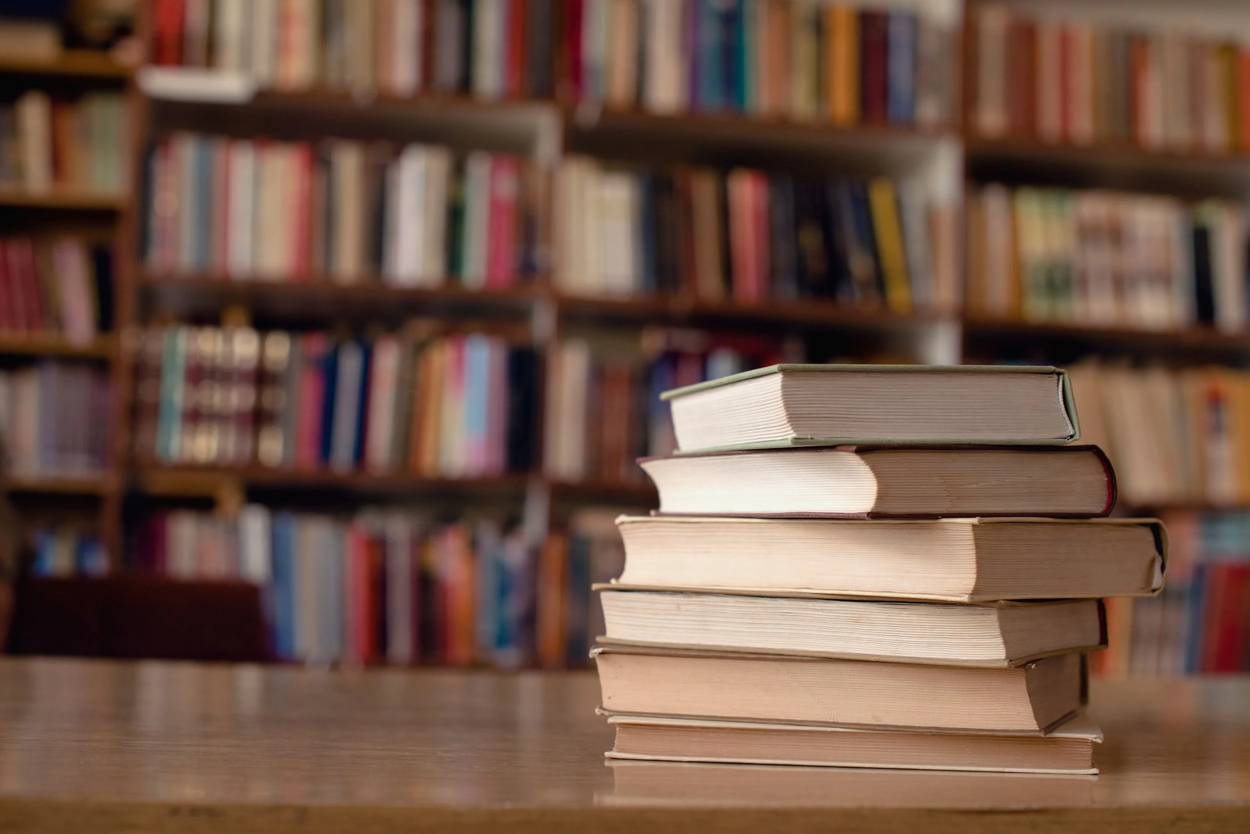 Stack of six books on a wooden table in a library