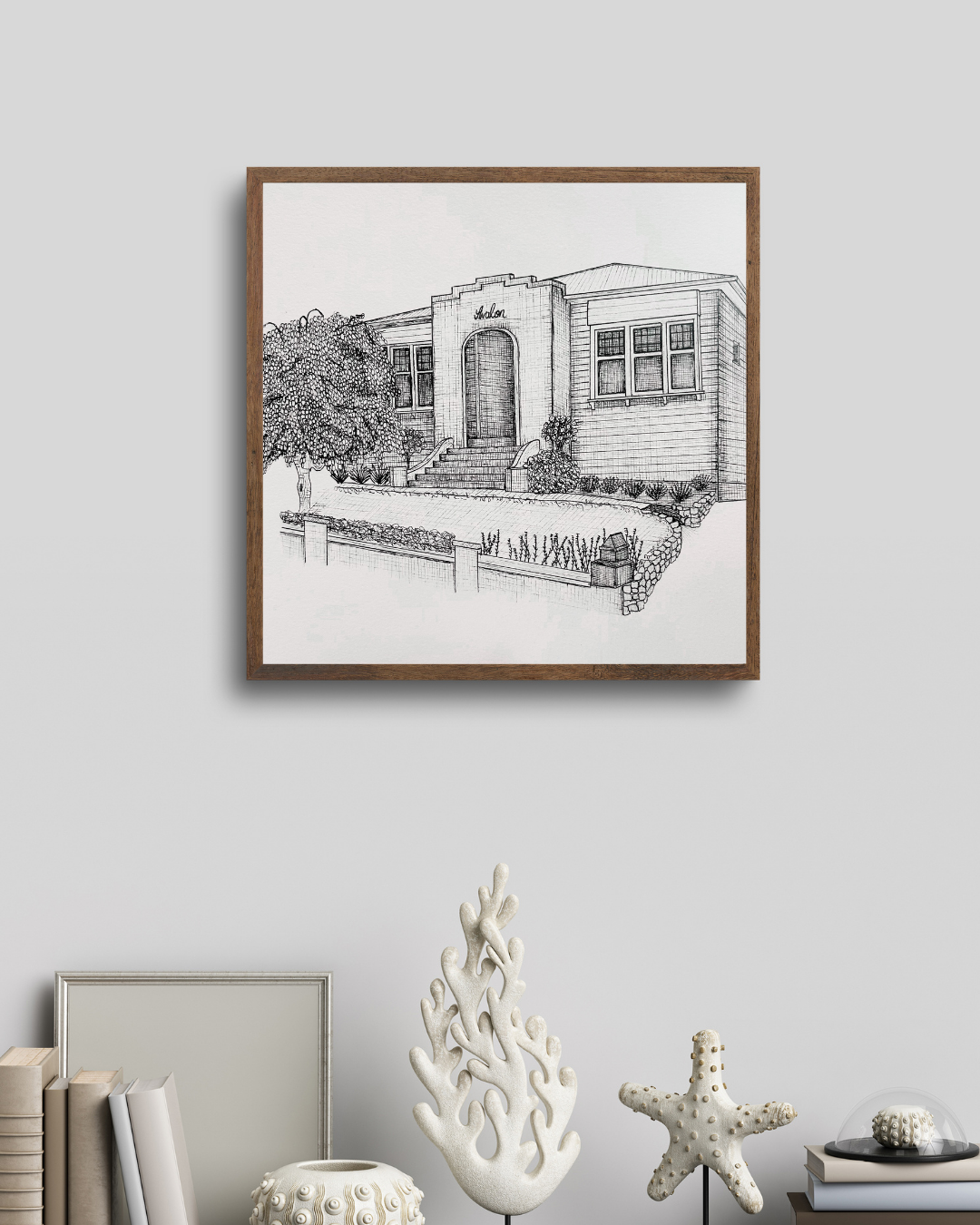 A framed black-and-white sketch of a house with stairs leading to the front door, a tree on the left, and a small garden in front.