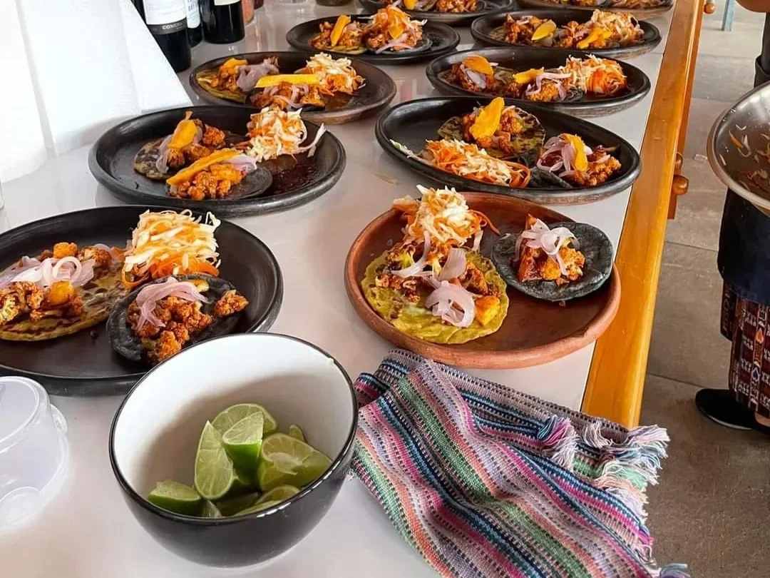 Multiple plates of tacos with meat, shredded cheese, onions, and jalapeños on a table.