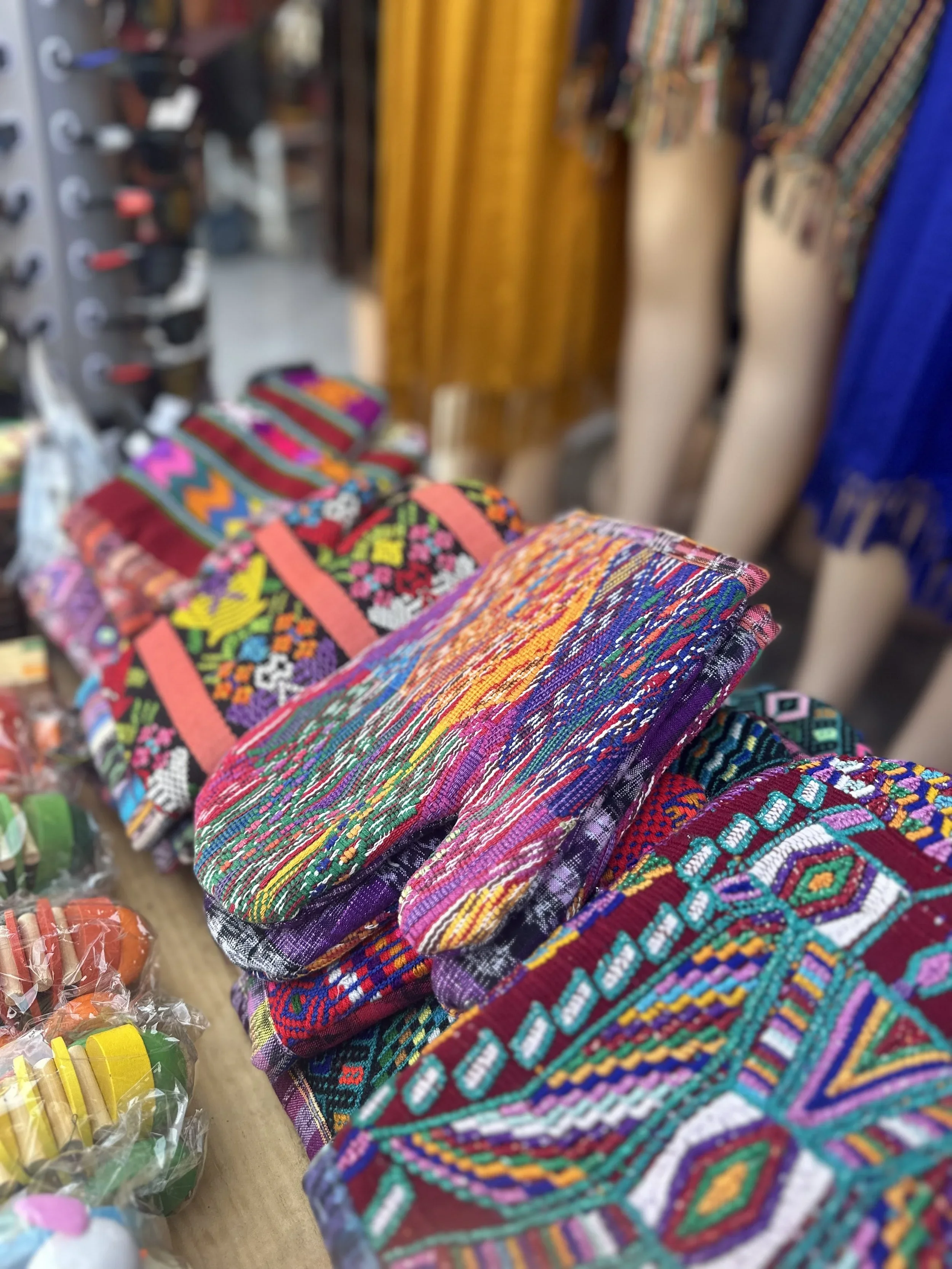 Colorful woven textiles and accessories, likely traditional Mexican embroidery, displayed on a market stall.