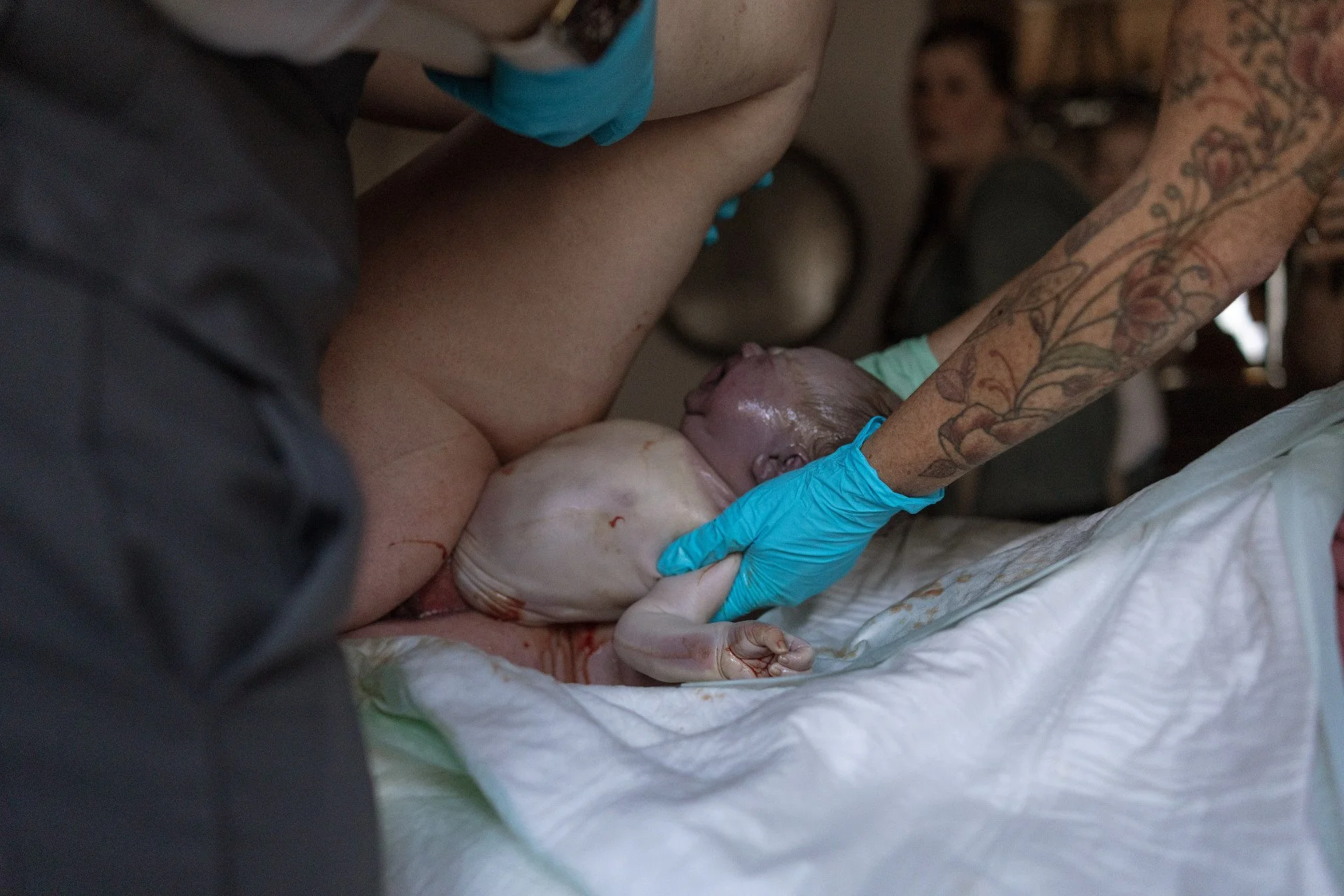 A person giving birth, with a newborn baby emerging from the mother. Medical gloves are worn by the person assisting.