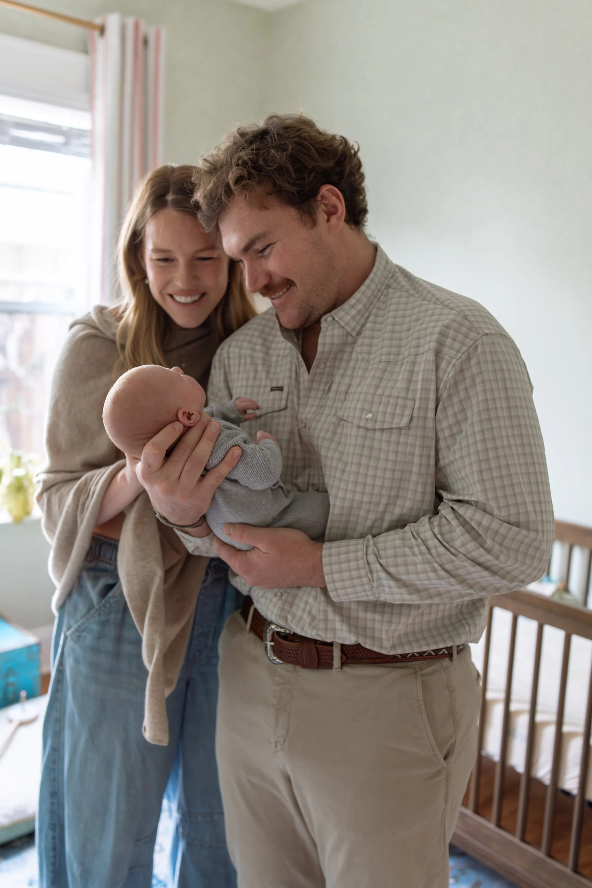 a woman and man stand together in a baby nursery smiling at their newborn baby boy in Austin Texas. 
