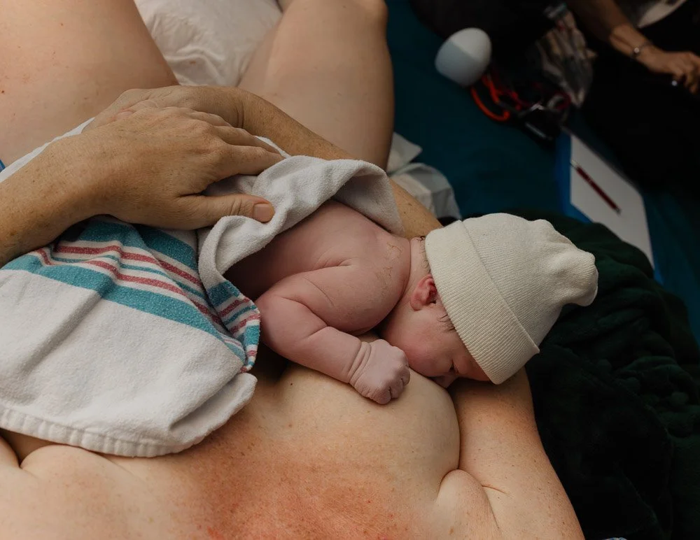 A newborn baby breastfeeding while wearing a beanie, held in a person's arms following a home water birth