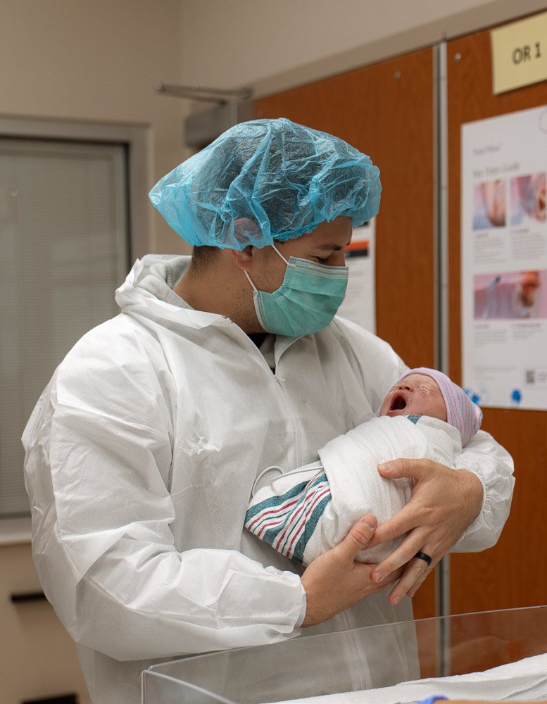 A healthcare worker in protective gear holding a newborn baby in a hospital setting.