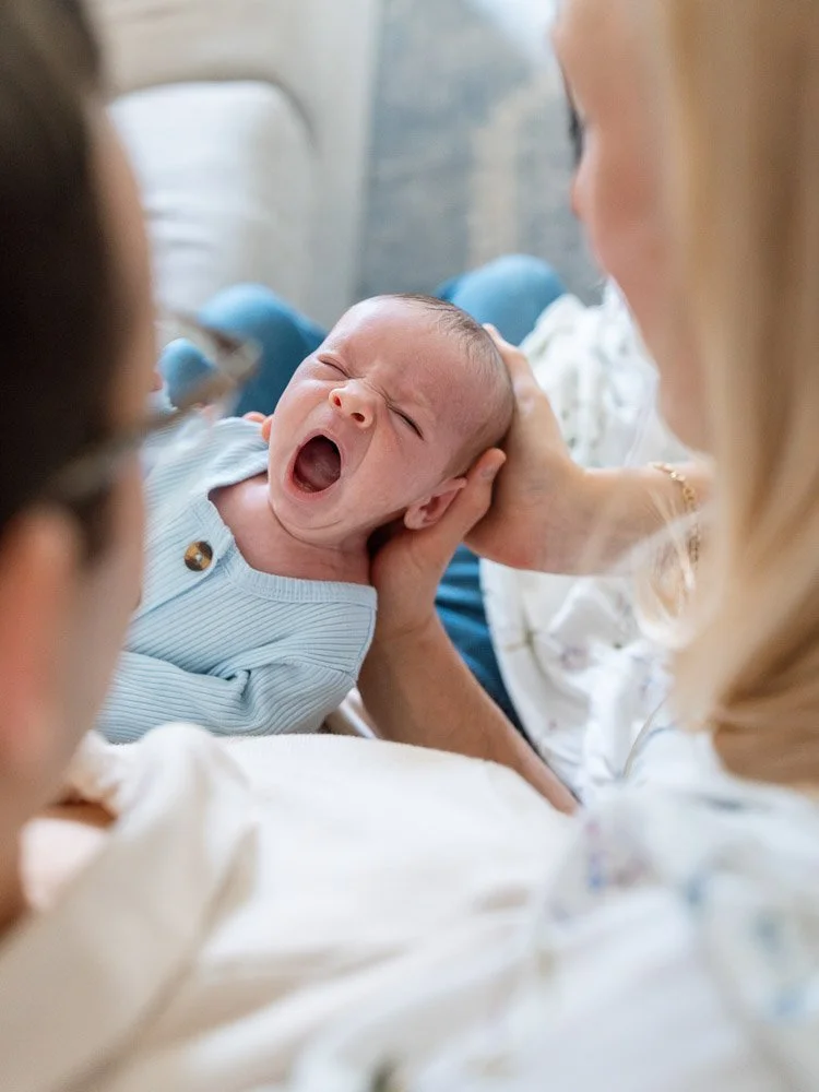 A newborn baby yawning while being held by a woman, surrounded by two other people in a hospital setting.