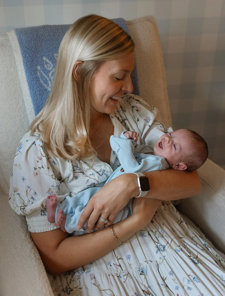 Woman with long blonde hair holding a crying baby boy on her lap while sitting on a beige armchair.