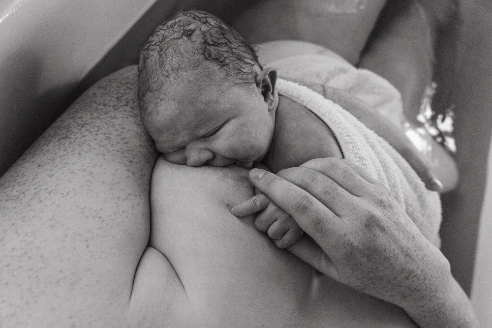 A newborn baby peacefully sleeping on a person's chest, with one hand gently touching the baby's head.