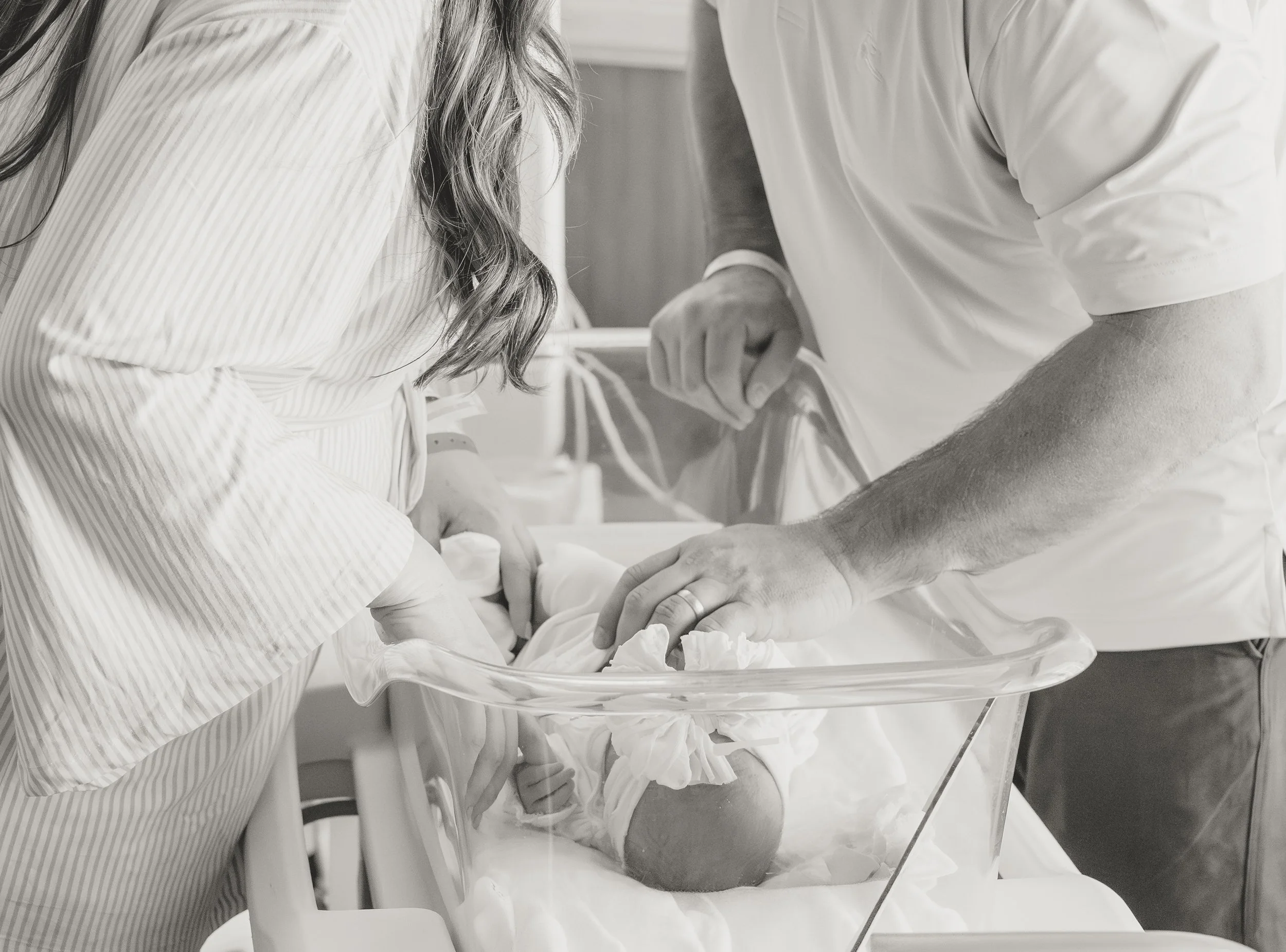 a woman and man lean over a hospital newborn bassinet that is holding a tiny baby. 